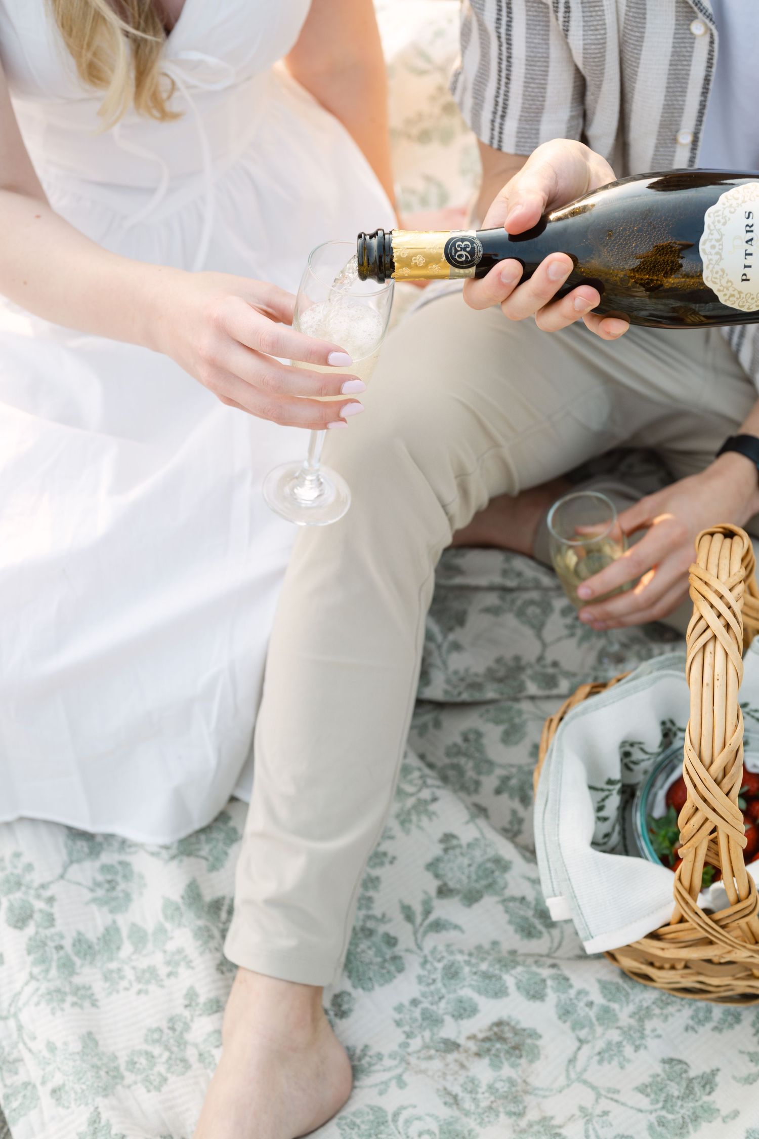 Details of champagne being poured on a floral patterned surface with wicker basket accents.