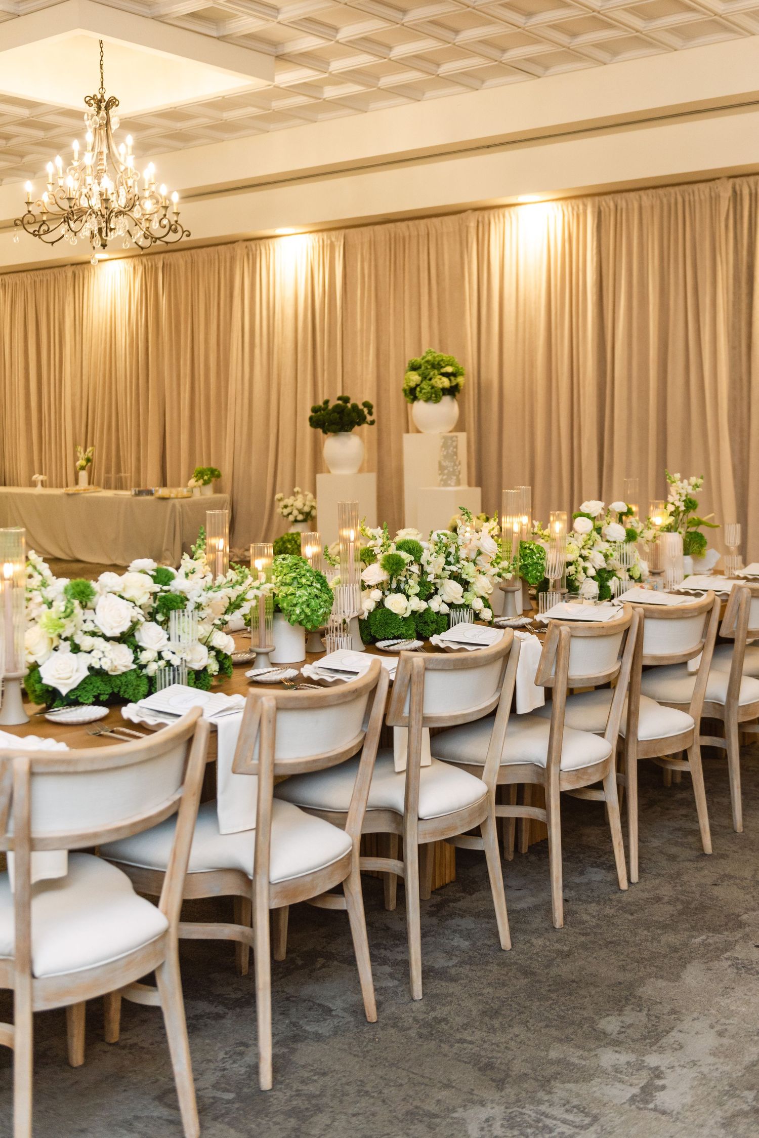 Luxurious banquet hall setup with wooden tables, upholstered chairs, and white floral arrangements.