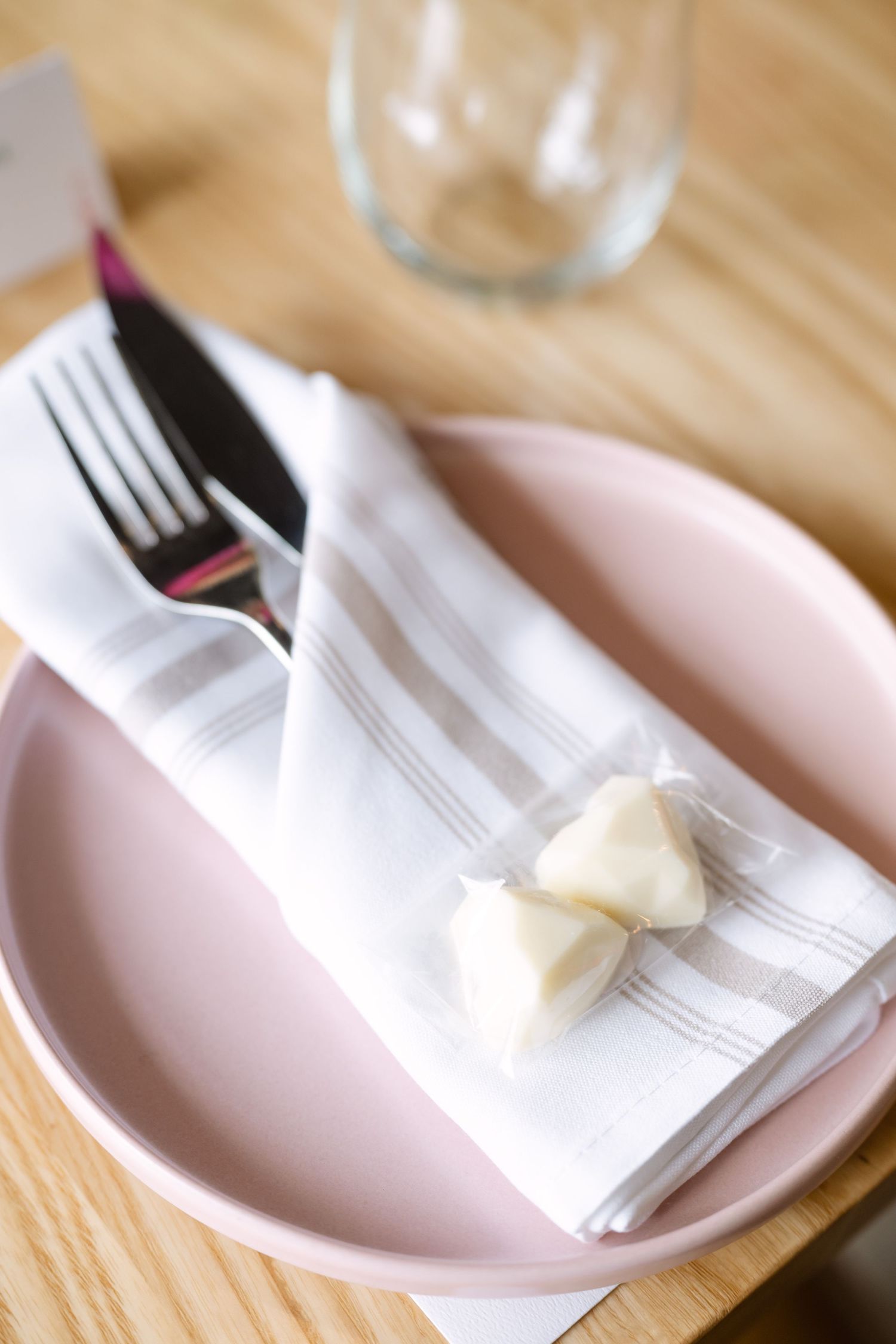 Pink plate with white striped napkin, fork, knife, and butter pats on a wooden restaurant table.