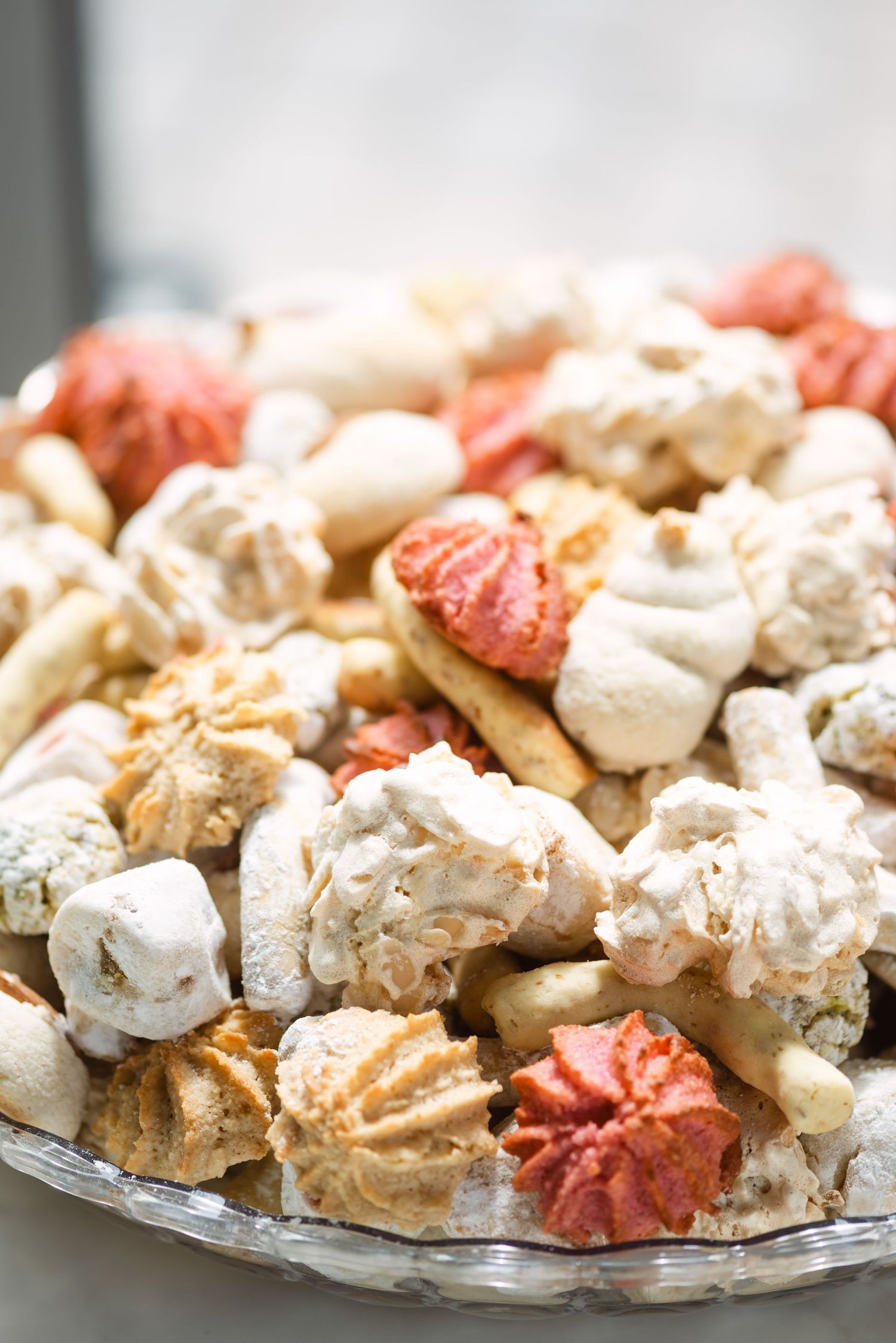 A glass plate piled high with assorted meringue cookies in white, cream, and red colors for a festive dessert display.