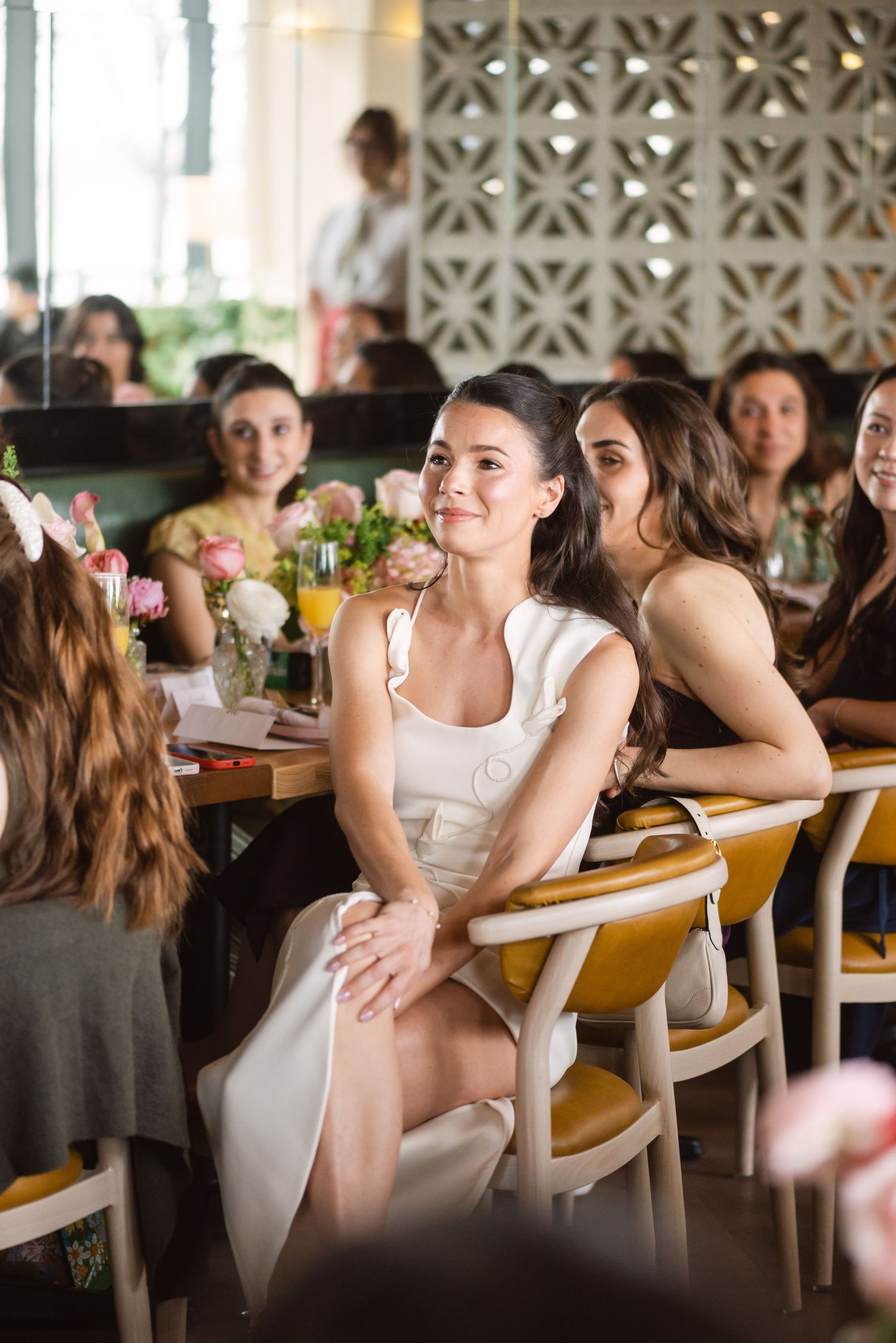 Bride in white dress sitting and smiling at wedding brunch reception with guests.