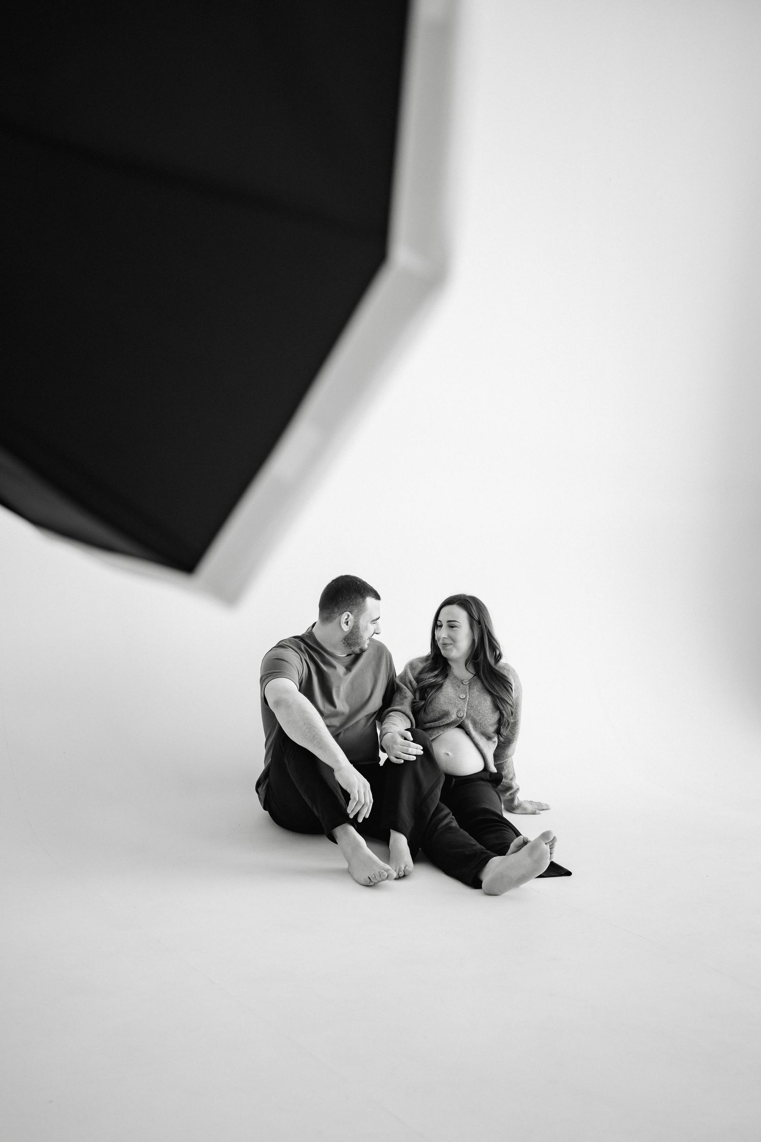 Artistic black and white photo sequence showing a couple lying down on a white backdrop in various poses.