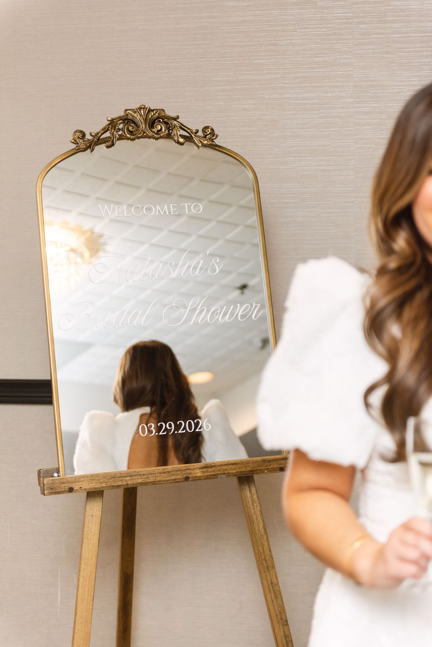 Gold ornate mirror on wooden easel displaying bridal shower welcome sign with date 03.29.2026, elegant event decor.