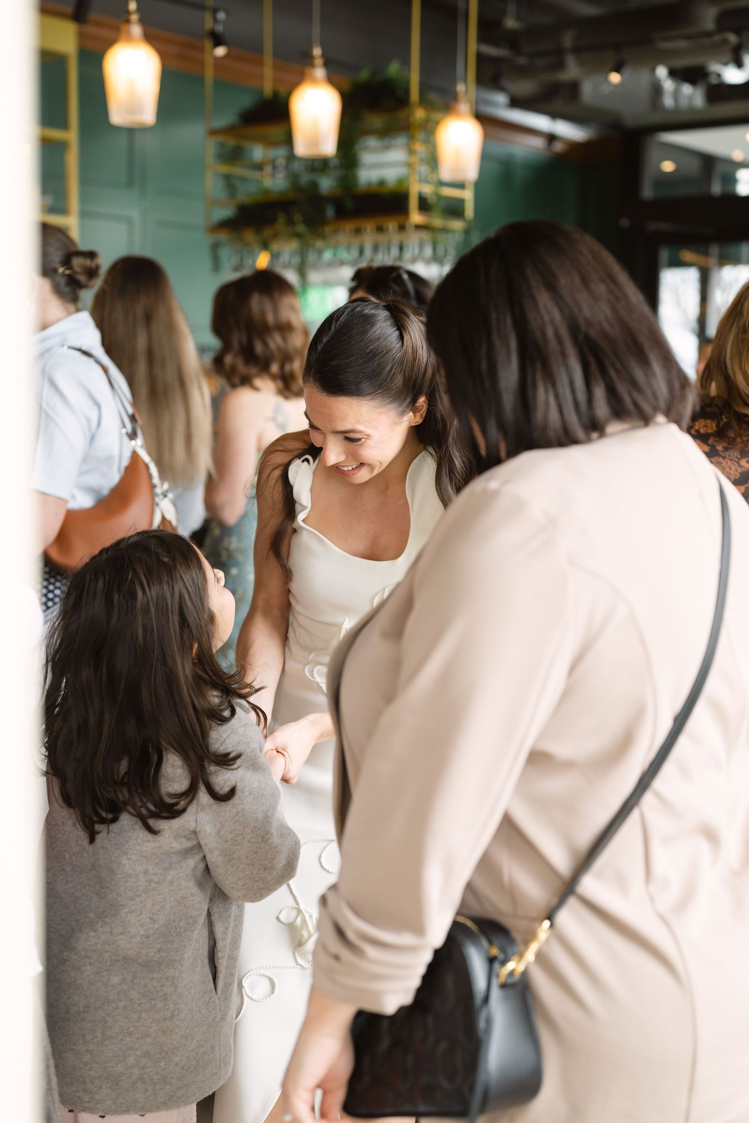 Bride in white dress smiling at a young child during a wedding reception in an elegant green restaurant.
