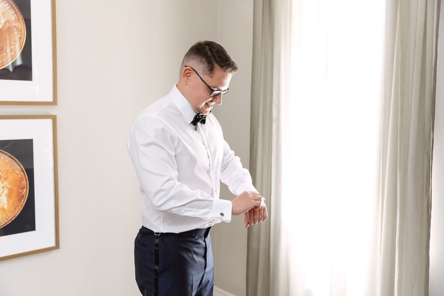 Groom in formal attire stands in front of curtained windows.