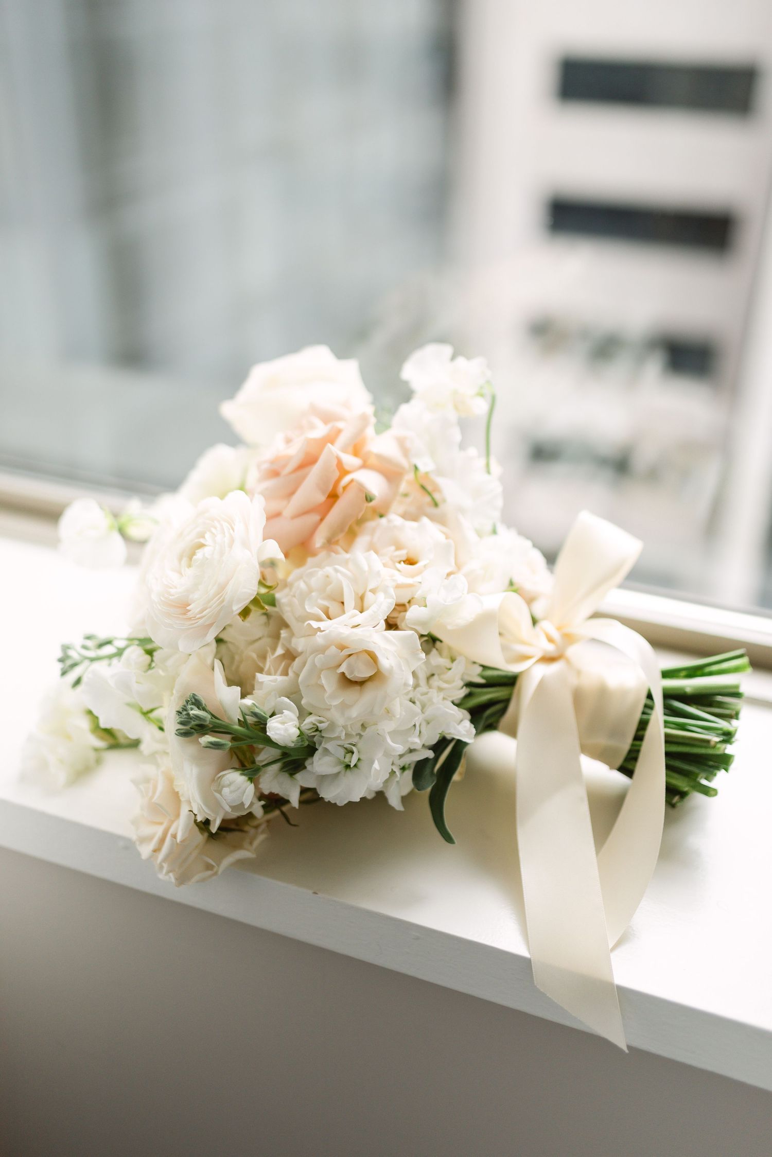 Delicate bridal bouquet with white and blush flowers tied with ivory ribbon.