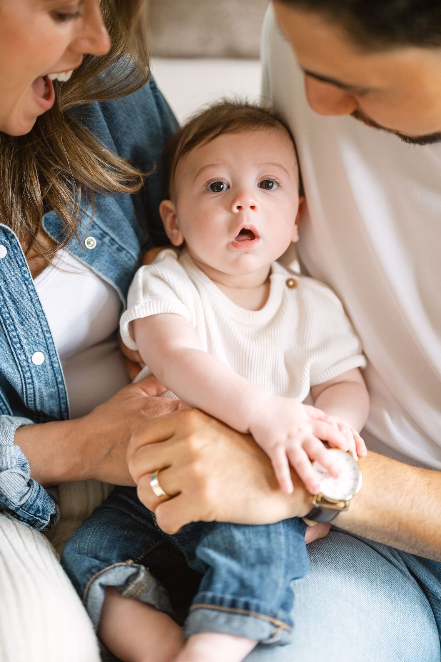 A series of intimate family moments showing parents holding and interacting with a baby in casual denim and white clothing.