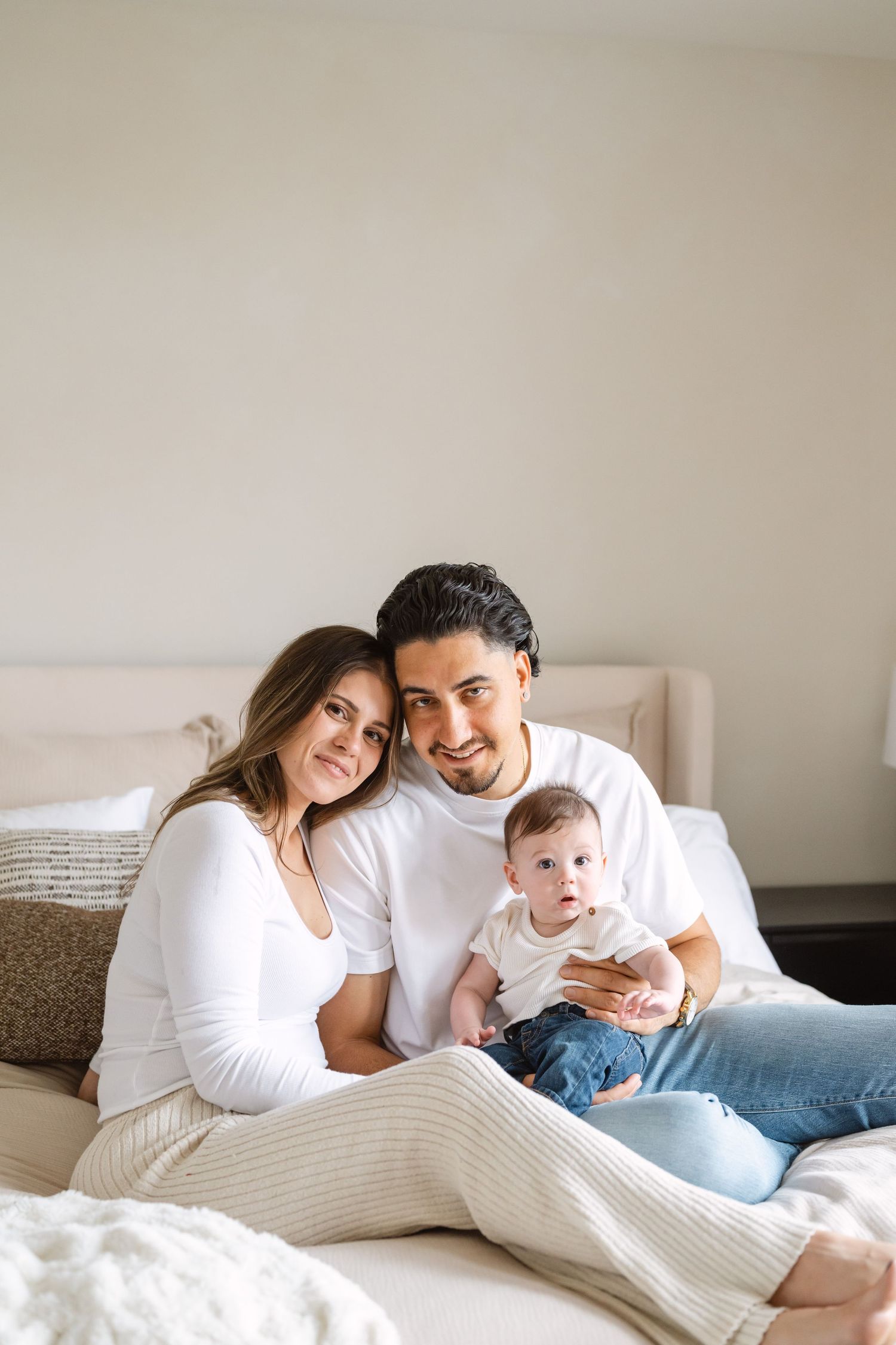 Family wearing white lounges together on cozy bed with textured bedding in soft natural light.