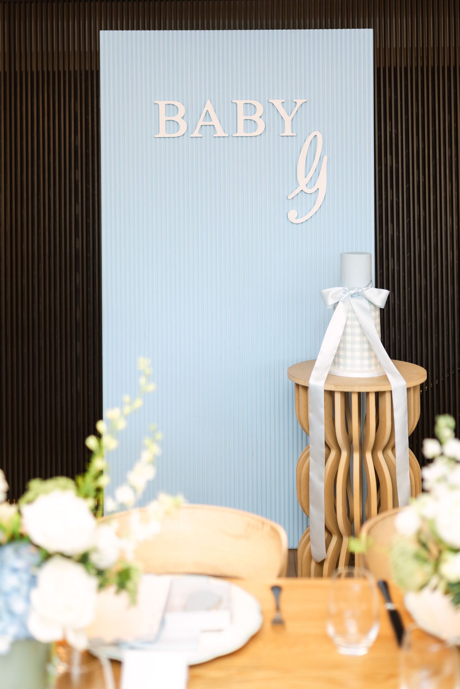 Elegant baby shower decoration with white text on blue background and wooden accents on a table setting.