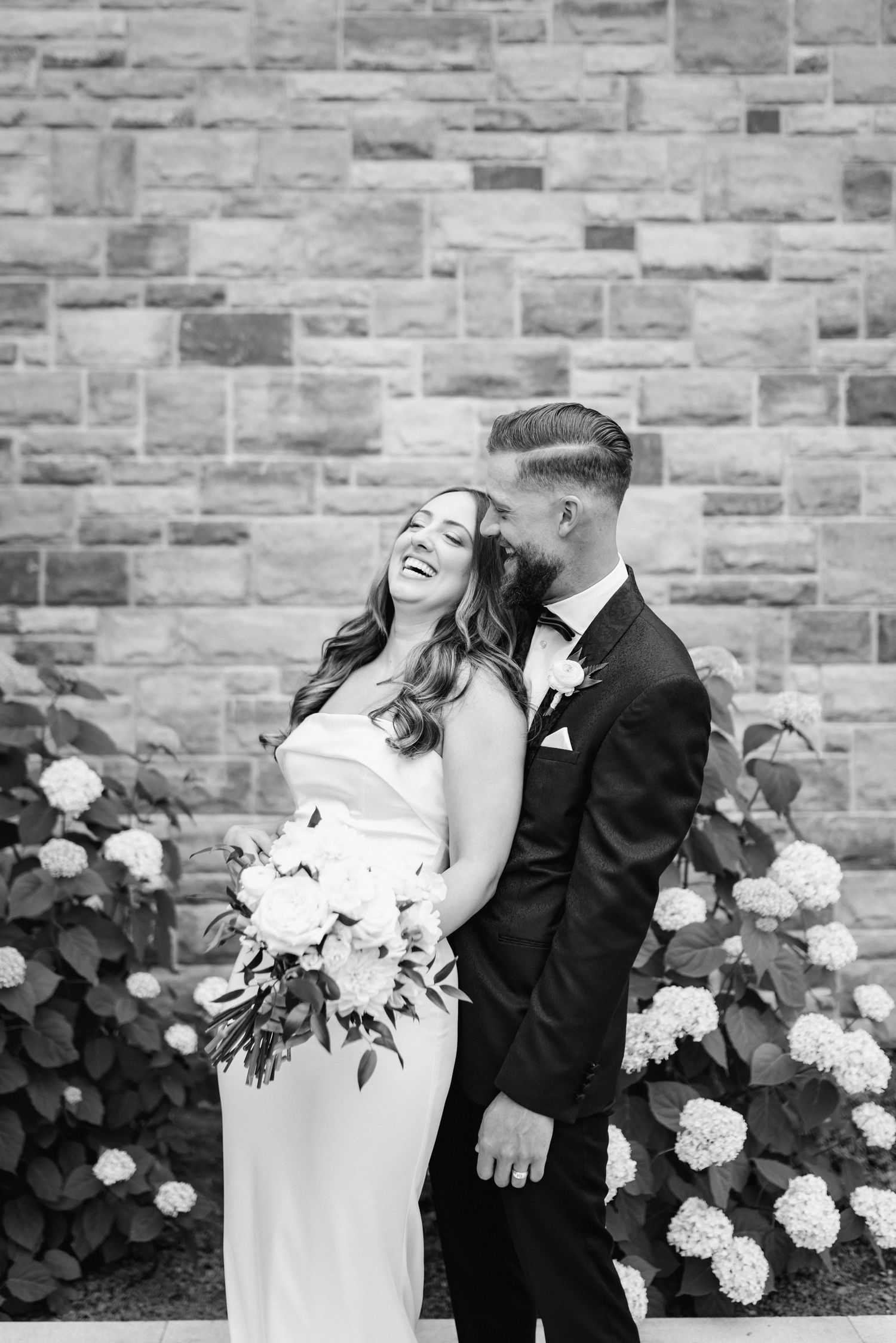 Romantic wedding portrait against a stone wall with blooming white hydrangeas.