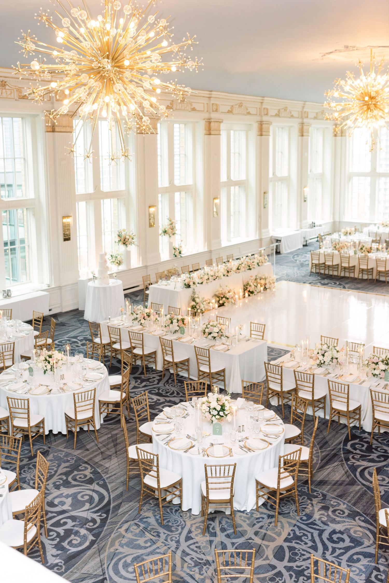 Stunning ballroom with starburst chandeliers and round tables arranged for an elegant wedding reception.