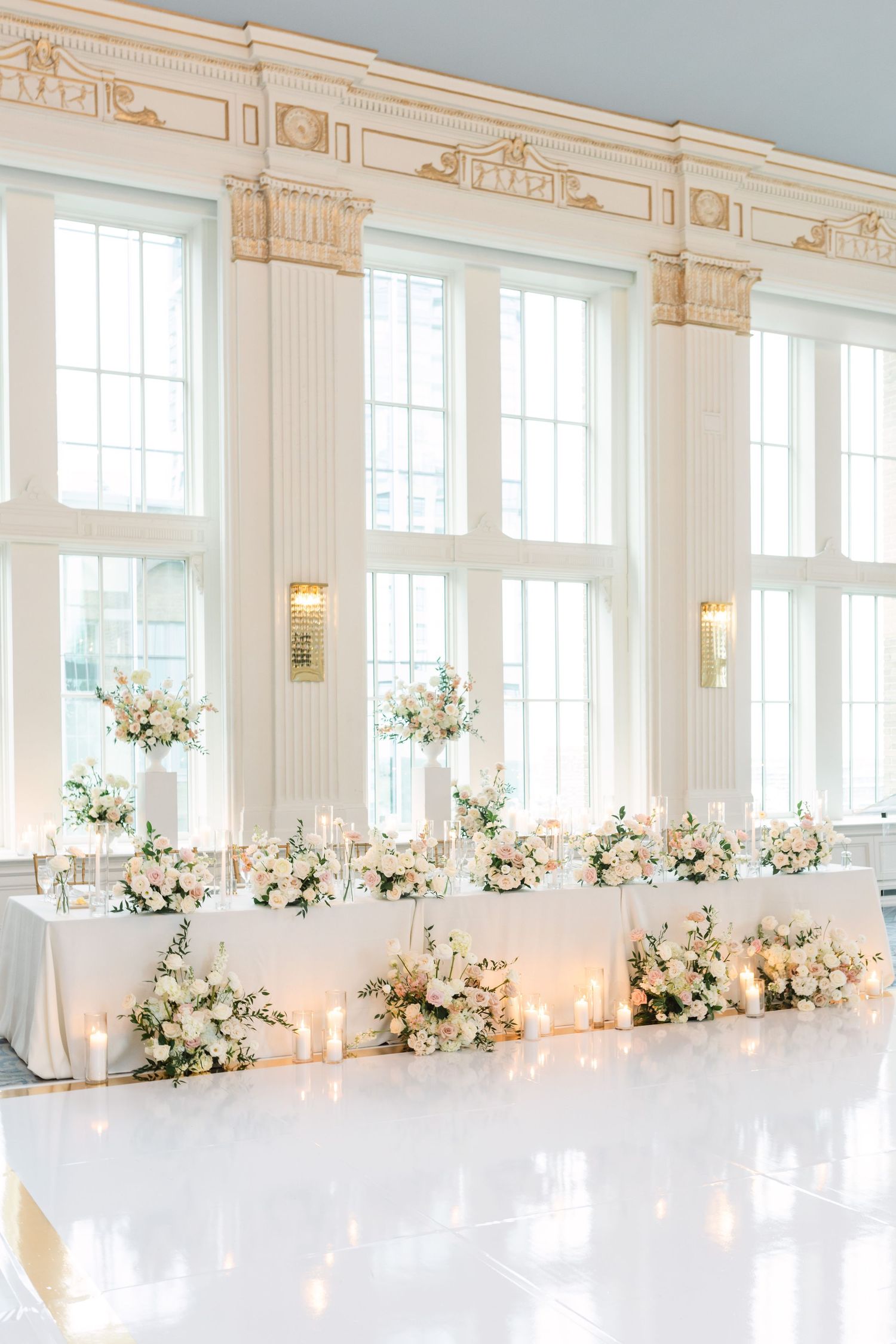 Bright ballroom decorated with classic white floral arrangements and tall windows.