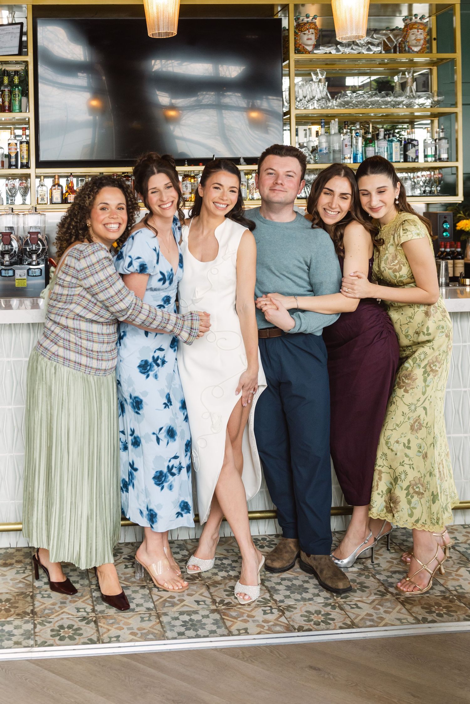 Group of five women and one man posing together smiling at a restaurant bar.