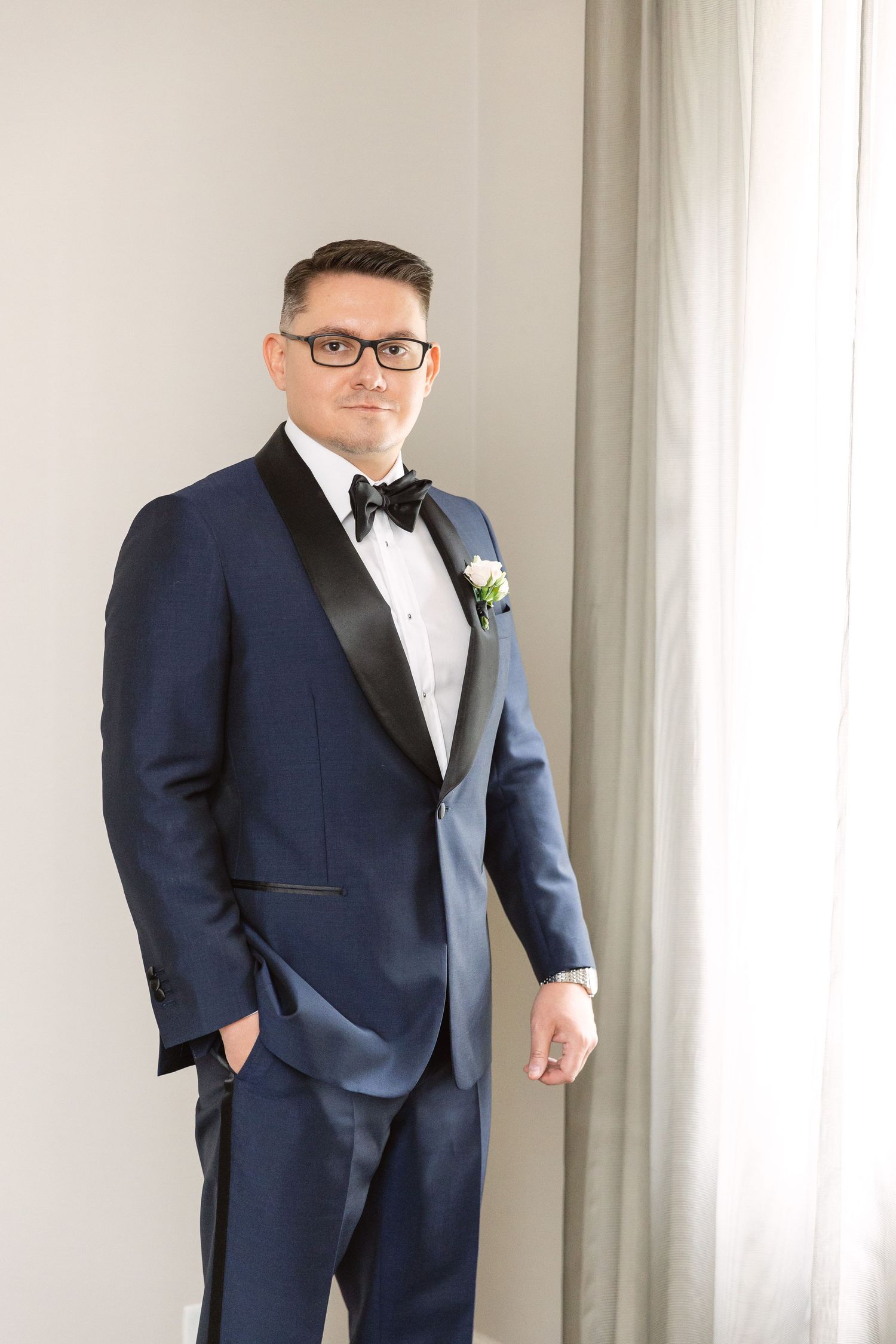 Groom poses in navy tuxedo with black lapels against light interior.