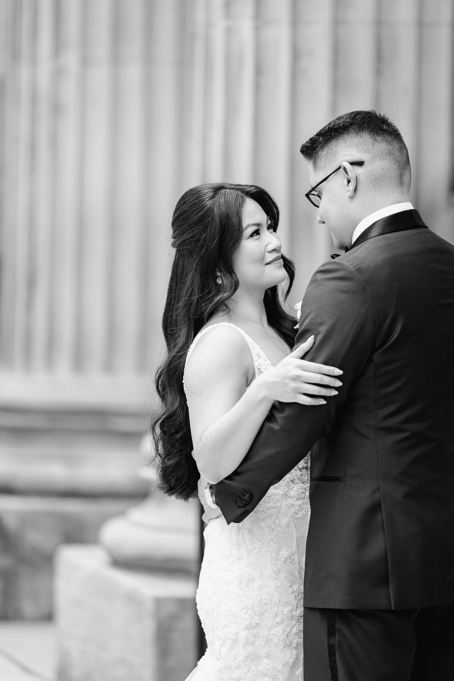 Intimate black and white portrait of newlyweds sharing a tender moment against white columns.