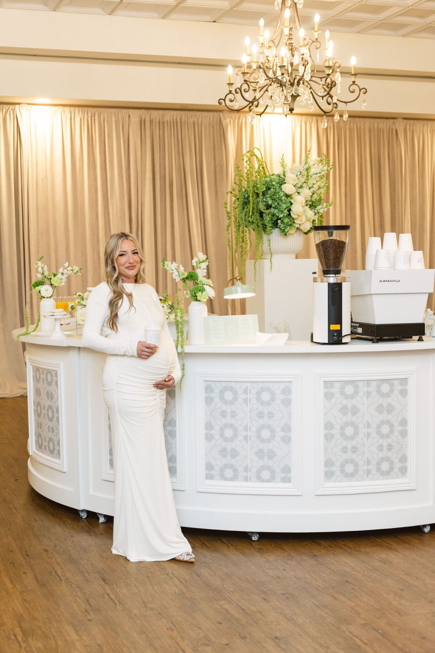 Elegant white curved bar setup with decorative panels and chandeliers in an event space.