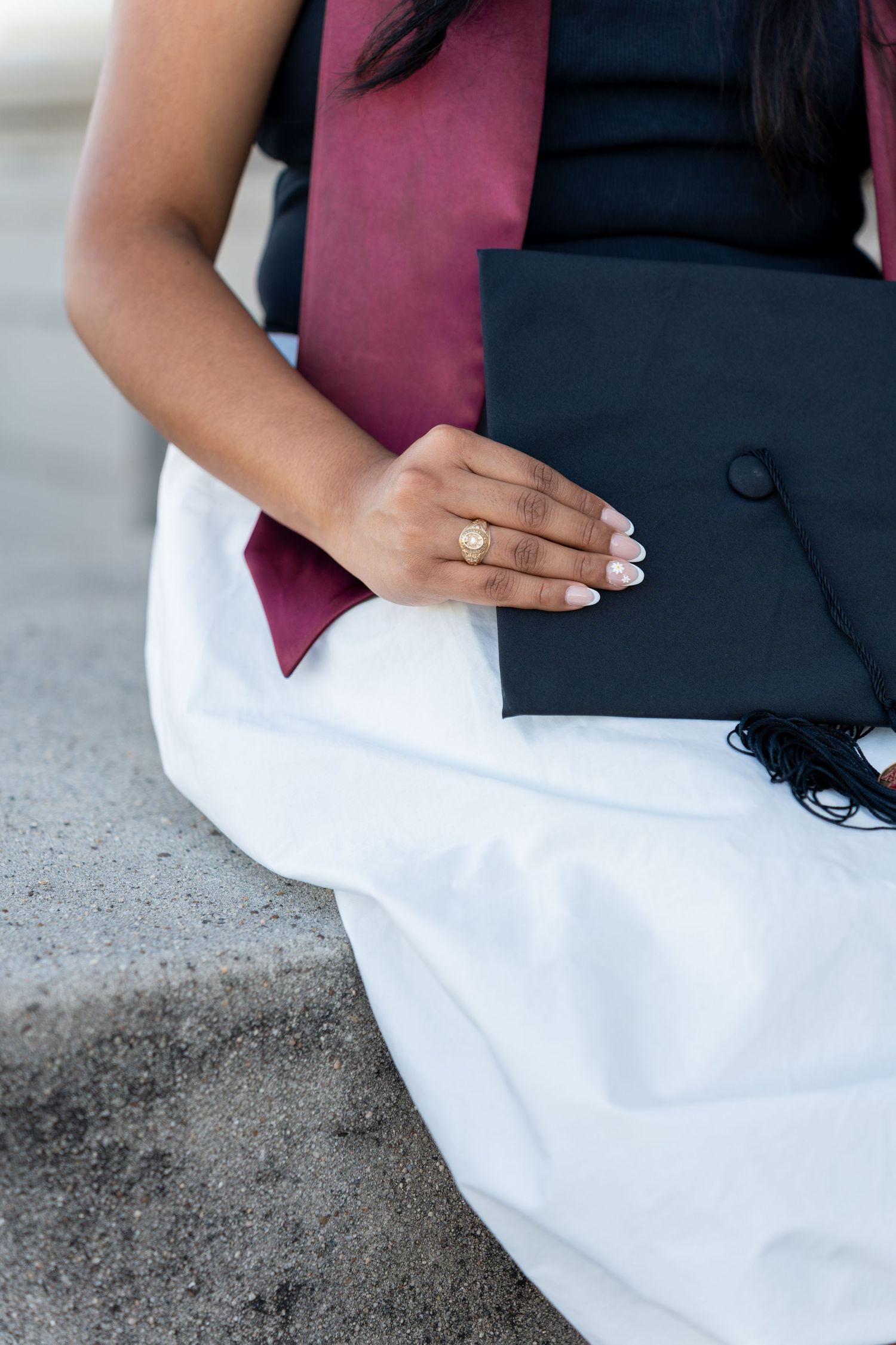 A person wearing a black and pink top sits on a concrete surface with white fabric draped across their lap.