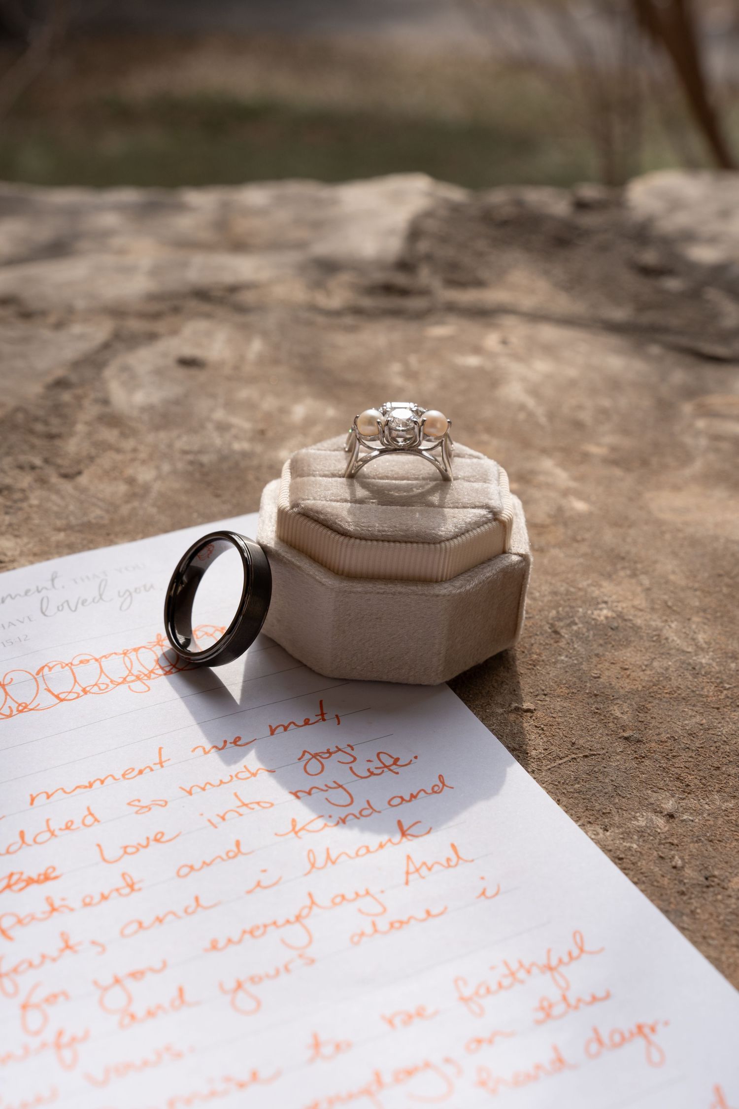 Wedding rings rest on handwritten love letters against a textured stone surface in natural lighting.