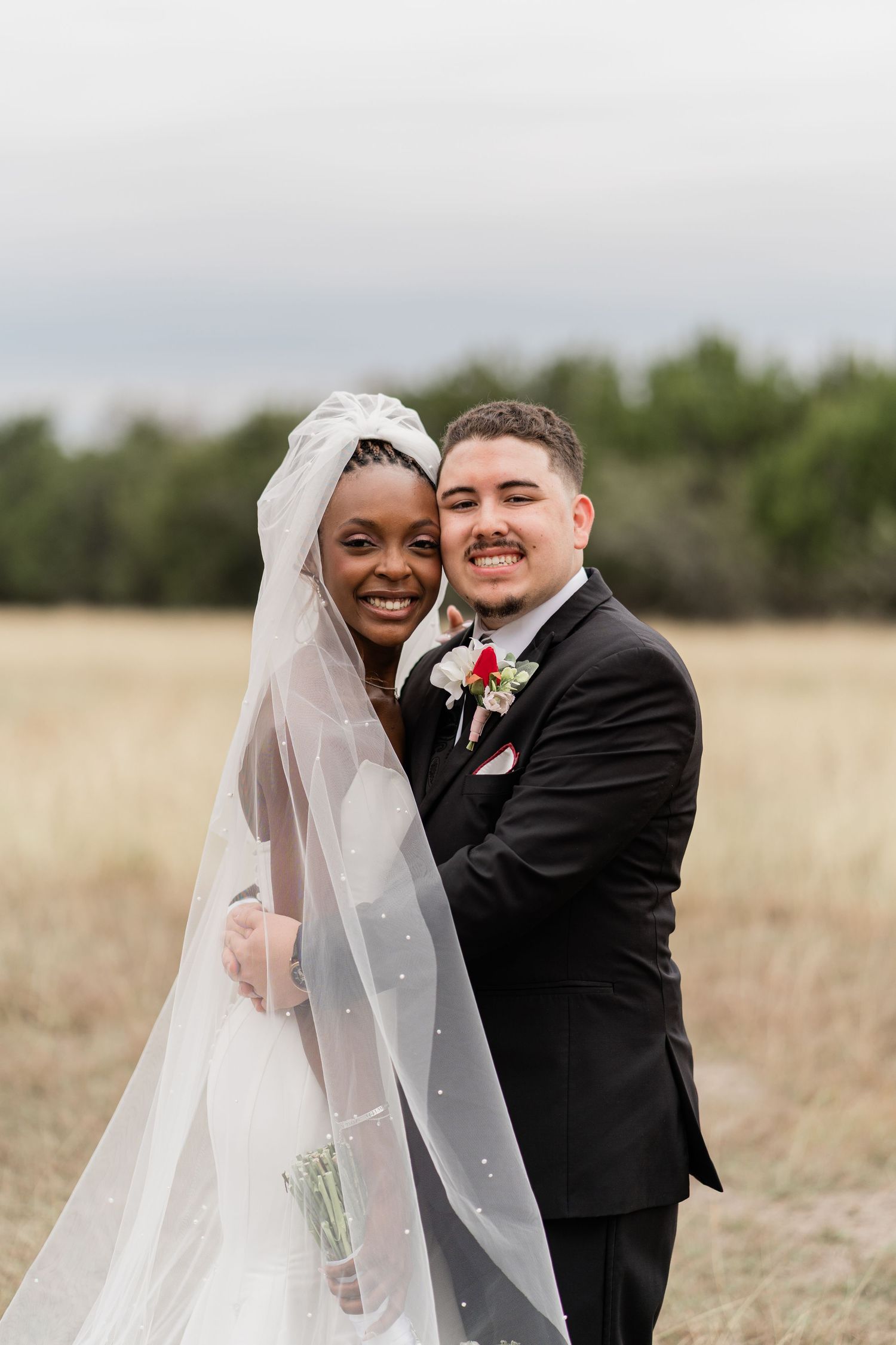 A joyful wedding couple shares intimate moments in an outdoor field setting with natural lighting and flowing veil.