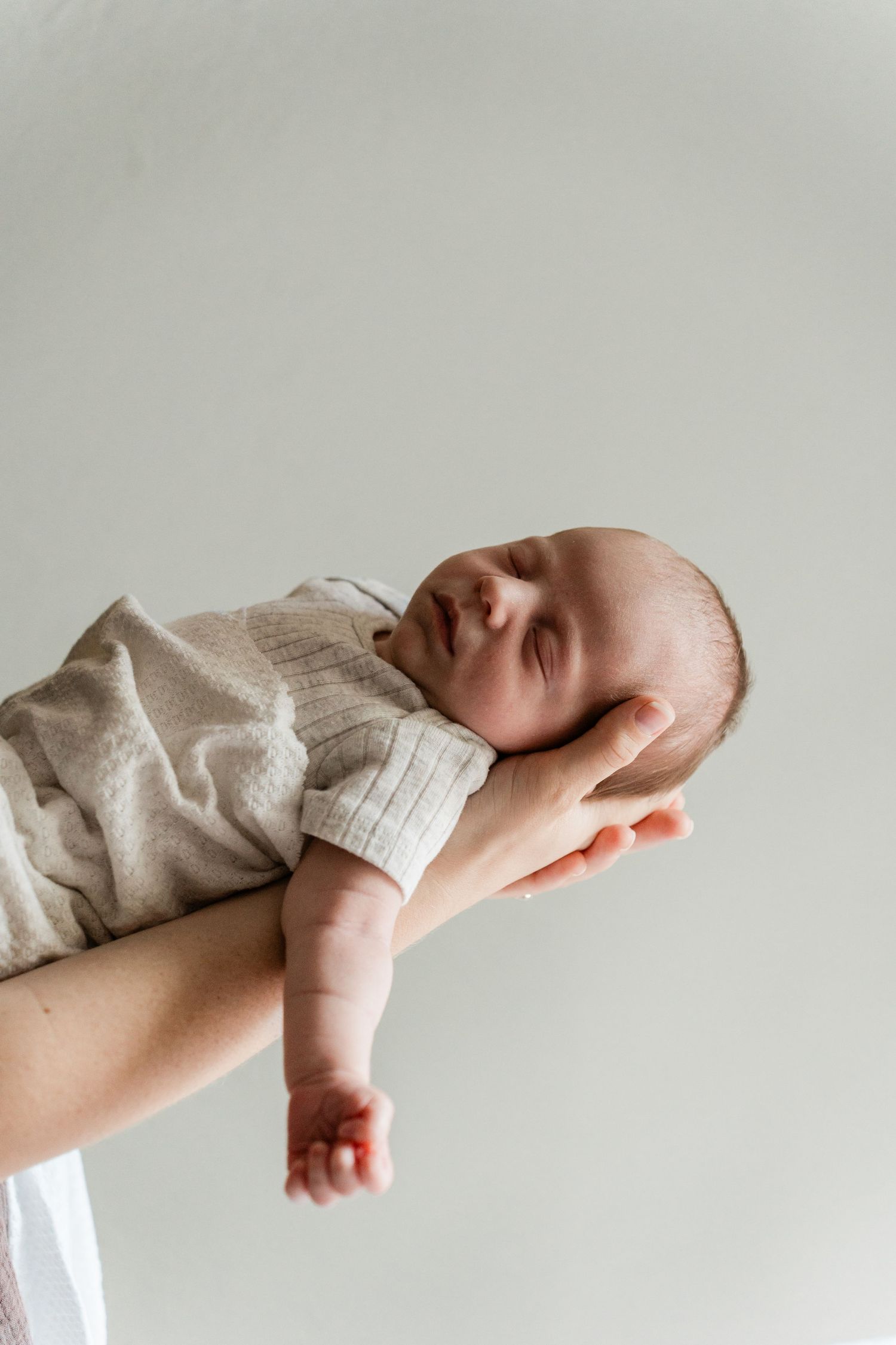 Minimalist portrait of sleeping newborn in neutral tones against light background.