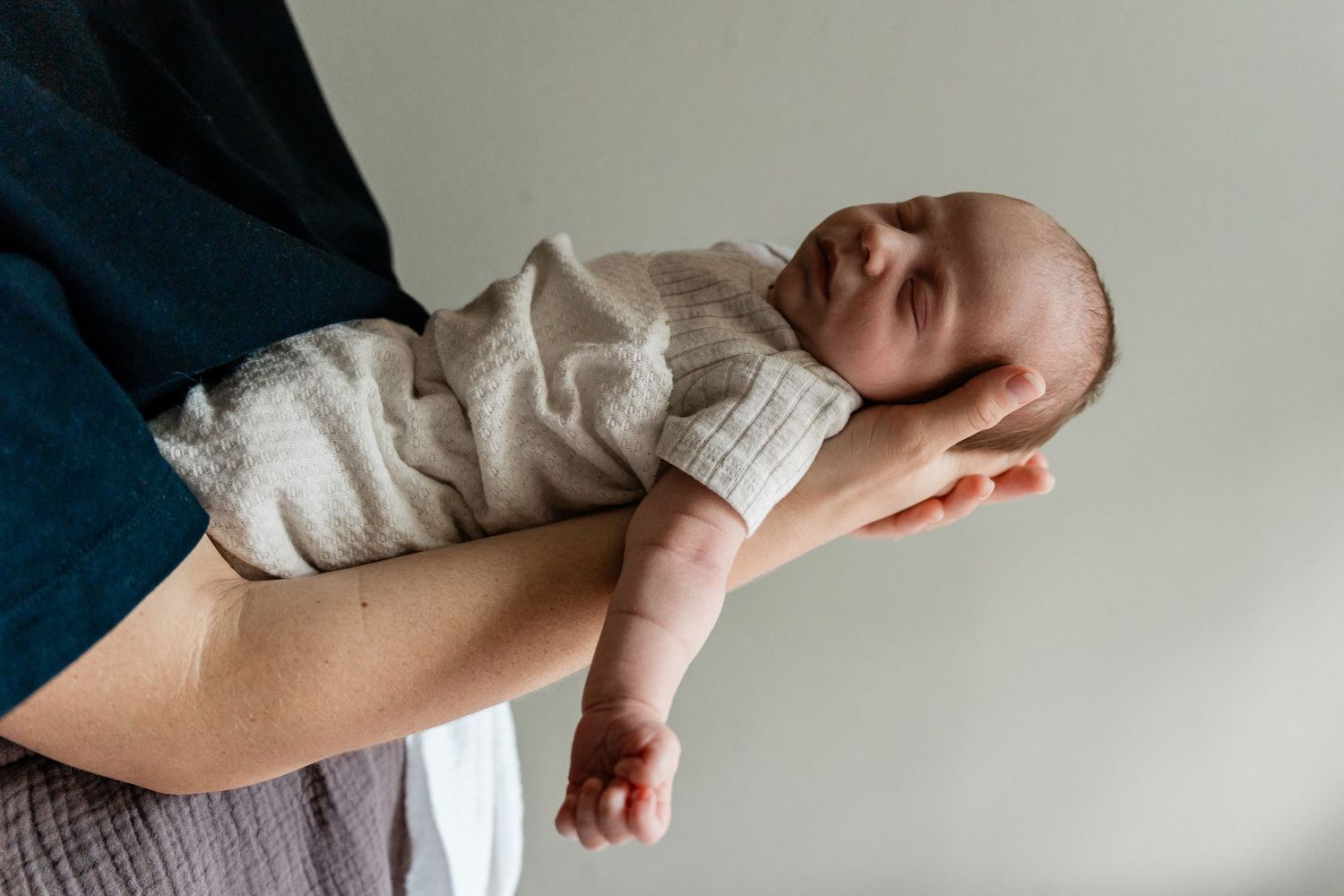 Peaceful newborn baby sleeping in soft white swaddle held in parent's arms.