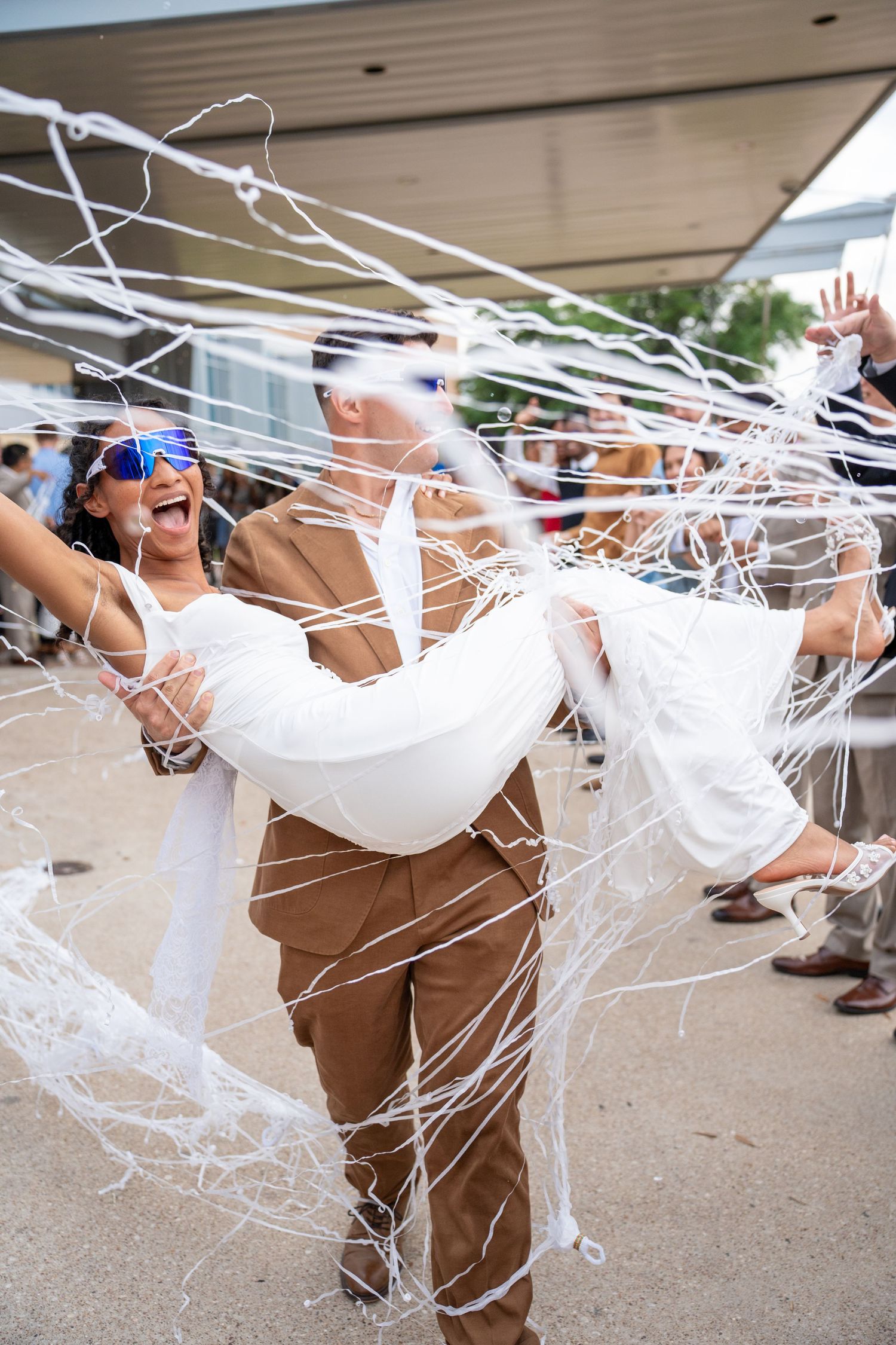 Wedding couple wrapped in white streamers during fun outdoor celebration.