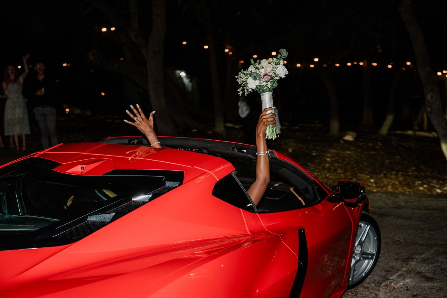 A bright red Ferrari sports car photographed at night with string lights visible in the background.