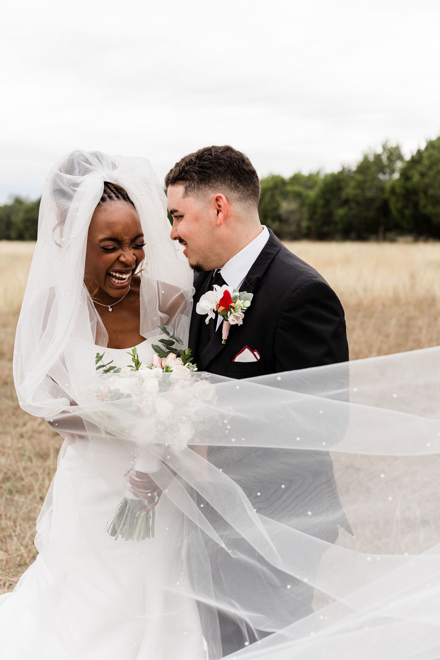 A joyful wedding couple shares a romantic moment as the bride's veil flows dramatically in the wind.