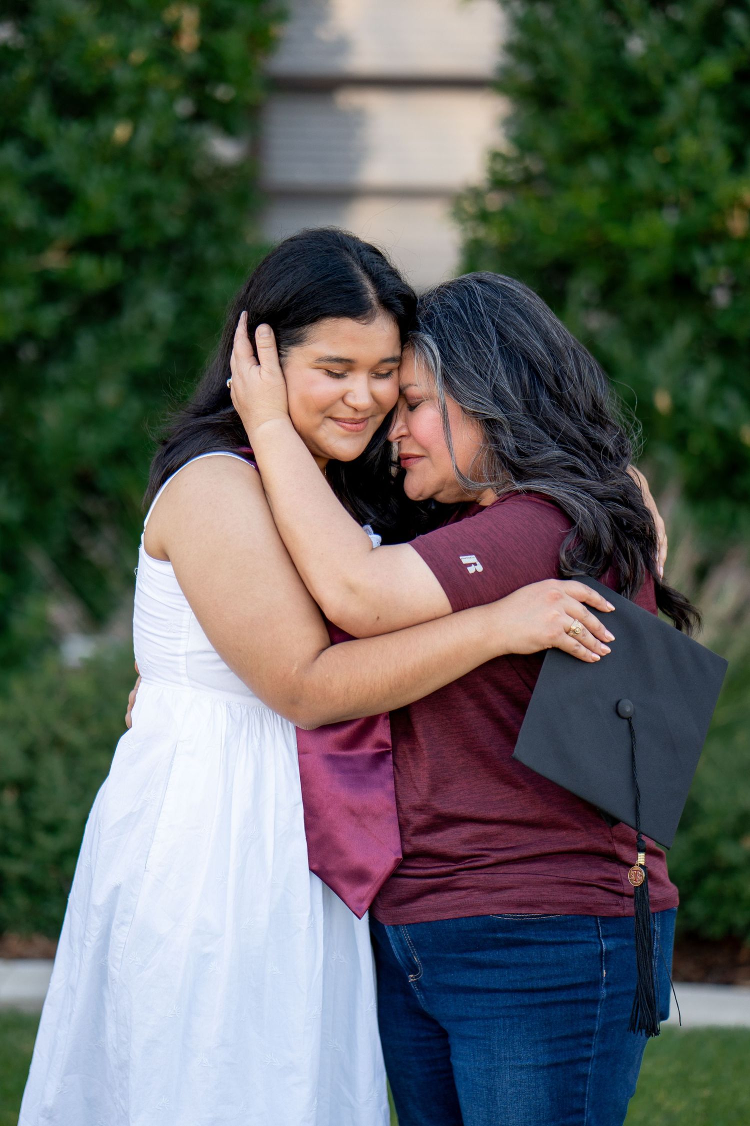 Two people share an intimate embrace outdoors against a backdrop of green foliage.