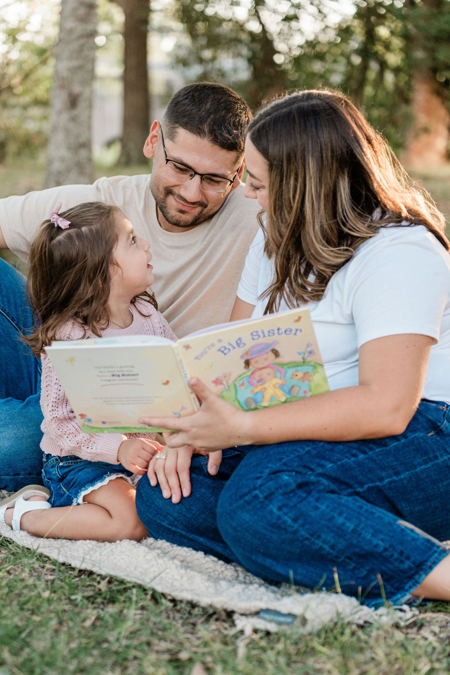 Family reading a children's book together while lying on a blue blanket in the grass.