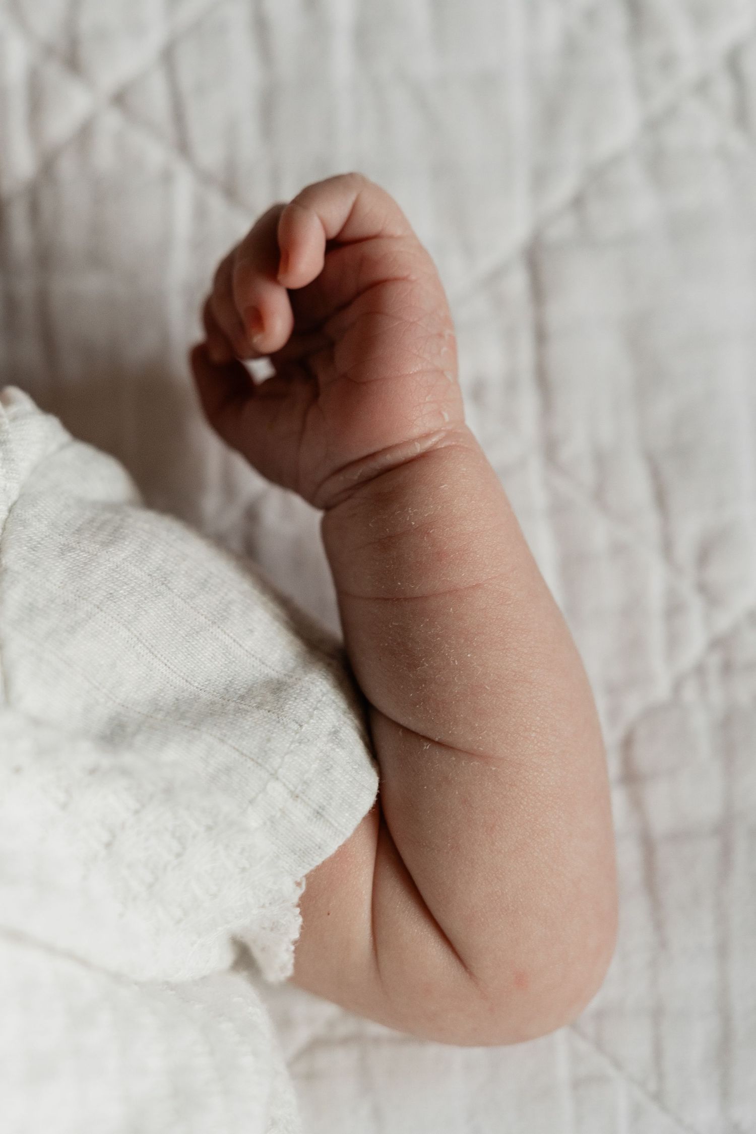 Close-up of tiny newborn baby fingers against white textured background.
