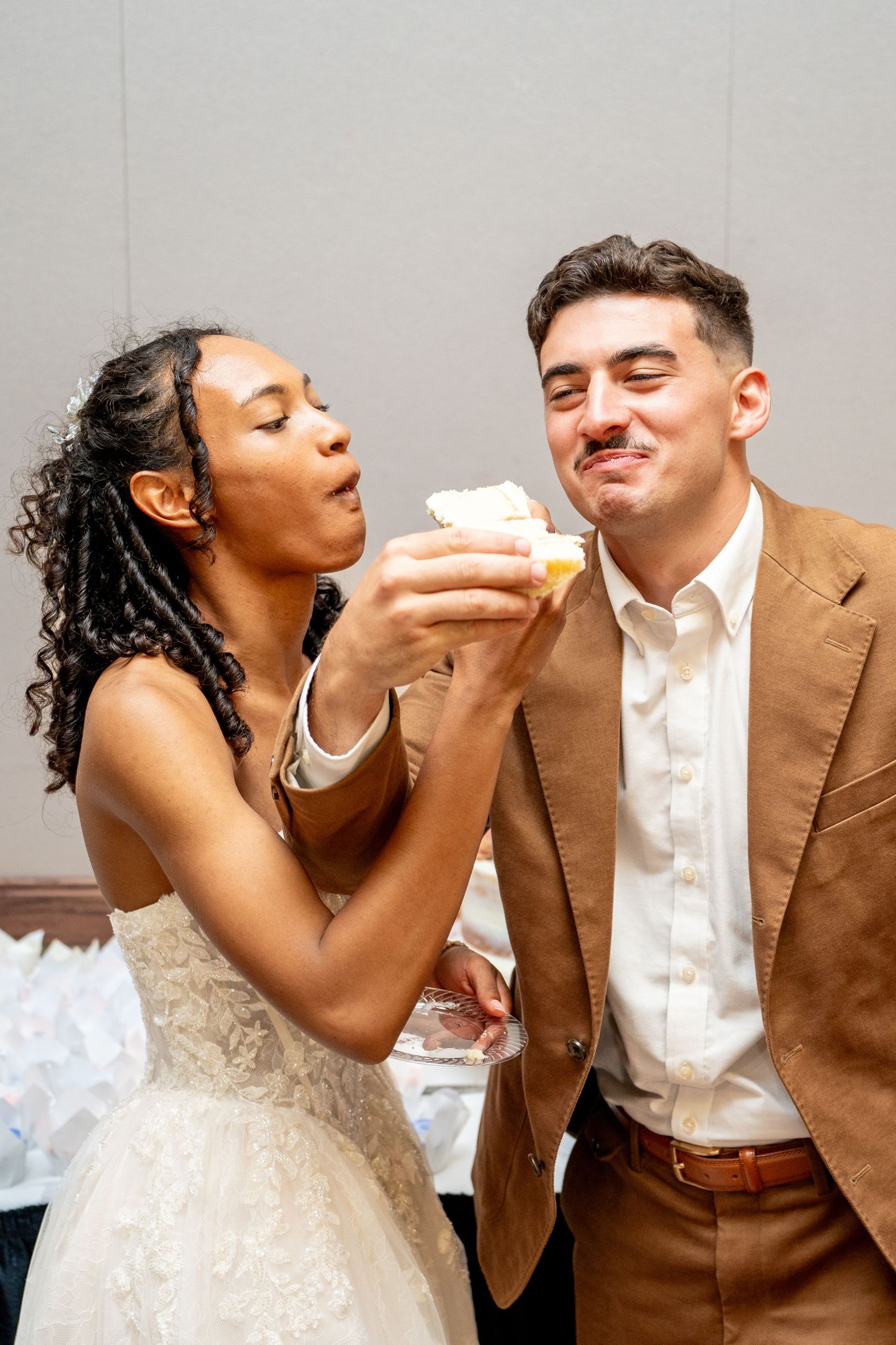 Playful couple sharing cake at their wedding reception.