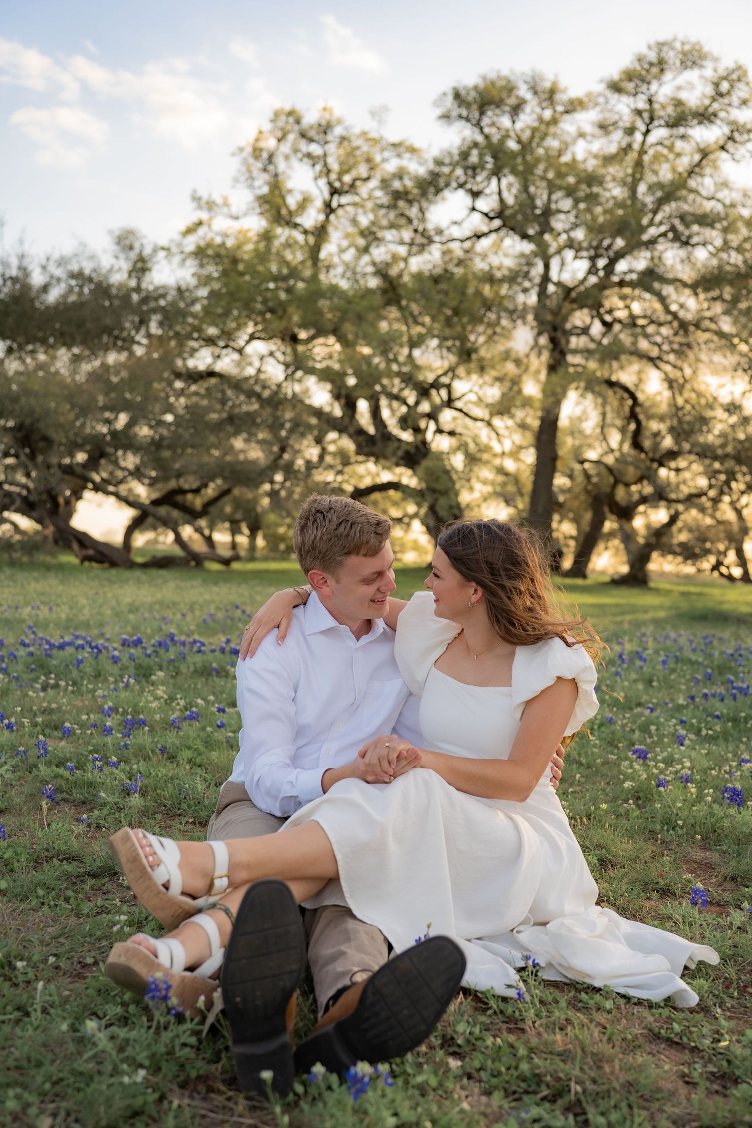A romantic couple lounges in a field of bluebonnets during golden hour sunset.
