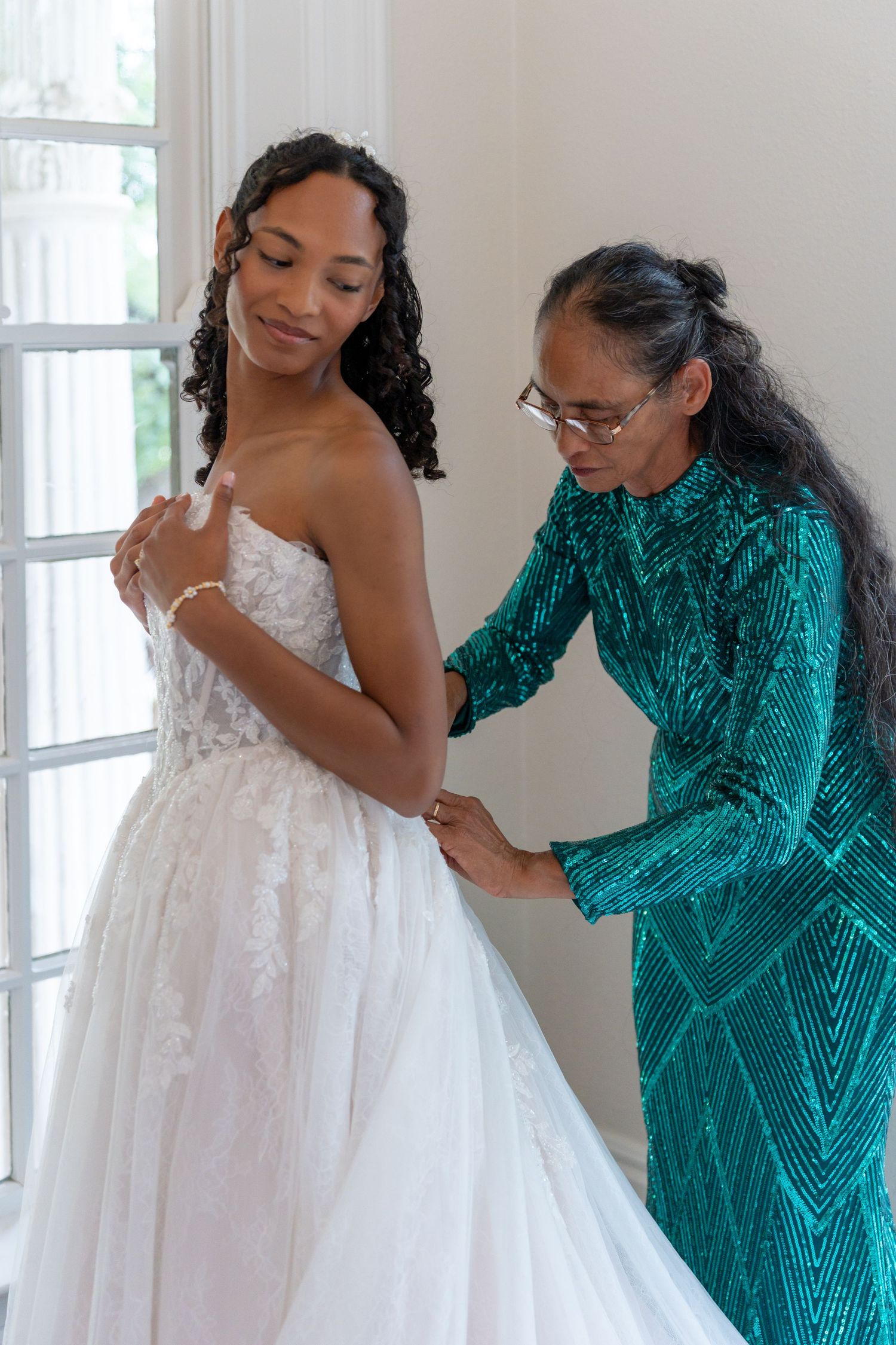 A wedding dress fitting session in a bright room with emerald green accents.
