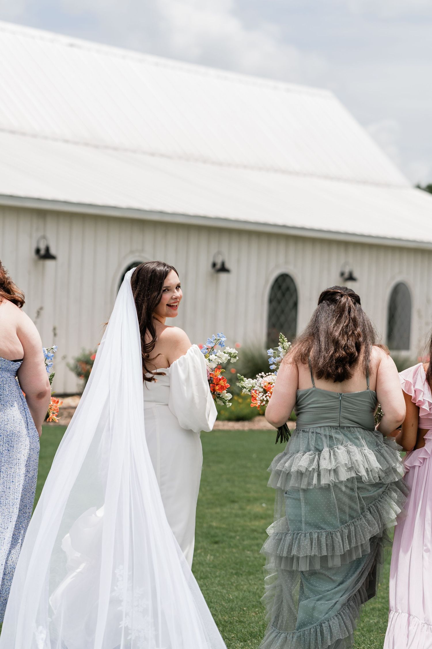 Candid moments of a wedding party enjoying themselves outside a rustic white barn.