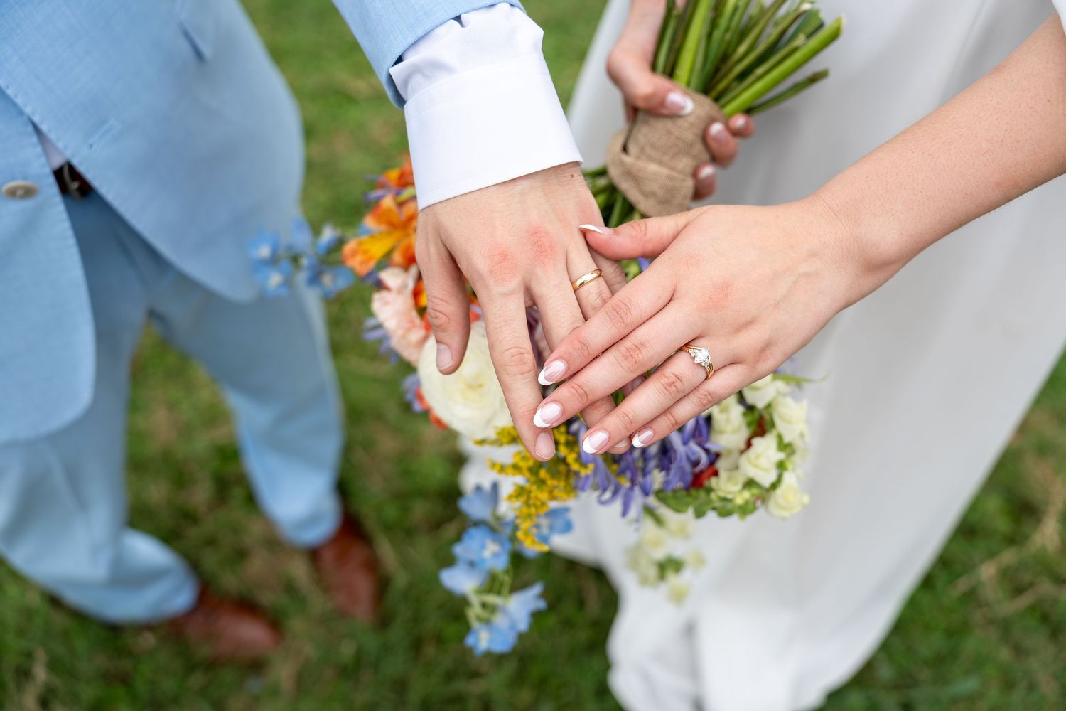 Close-up of newlyweds' hands with rings and delicate wildflower bouquet.