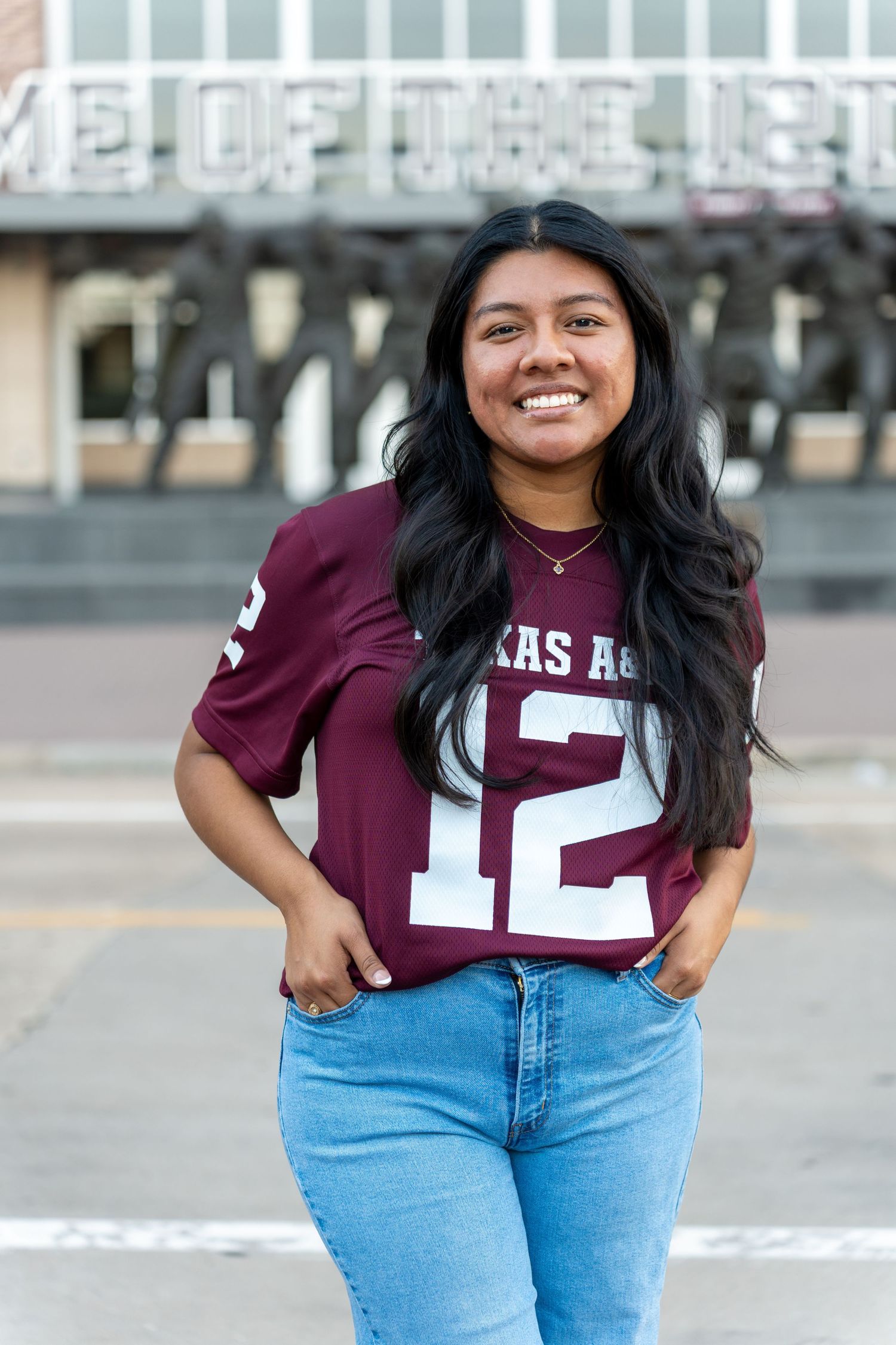 Someone wearing a maroon Texas A&M jersey and light blue jeans poses casually outdoors.
