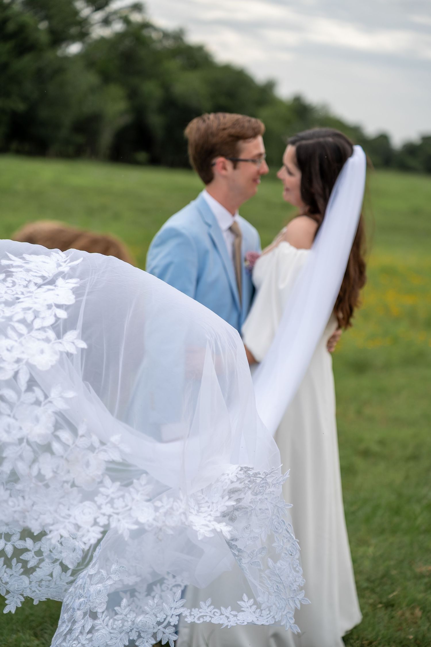 Delicate lace details of a wedding veil flutter in the breeze against a pastoral background.