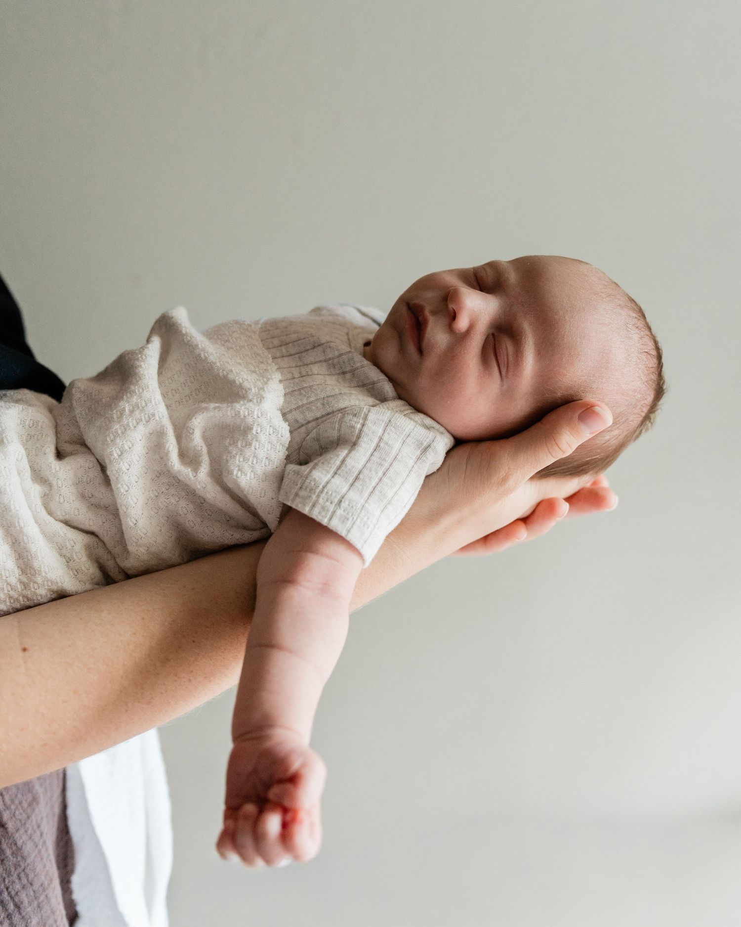 Gentle close-up of newborn baby's arm against neutral background.