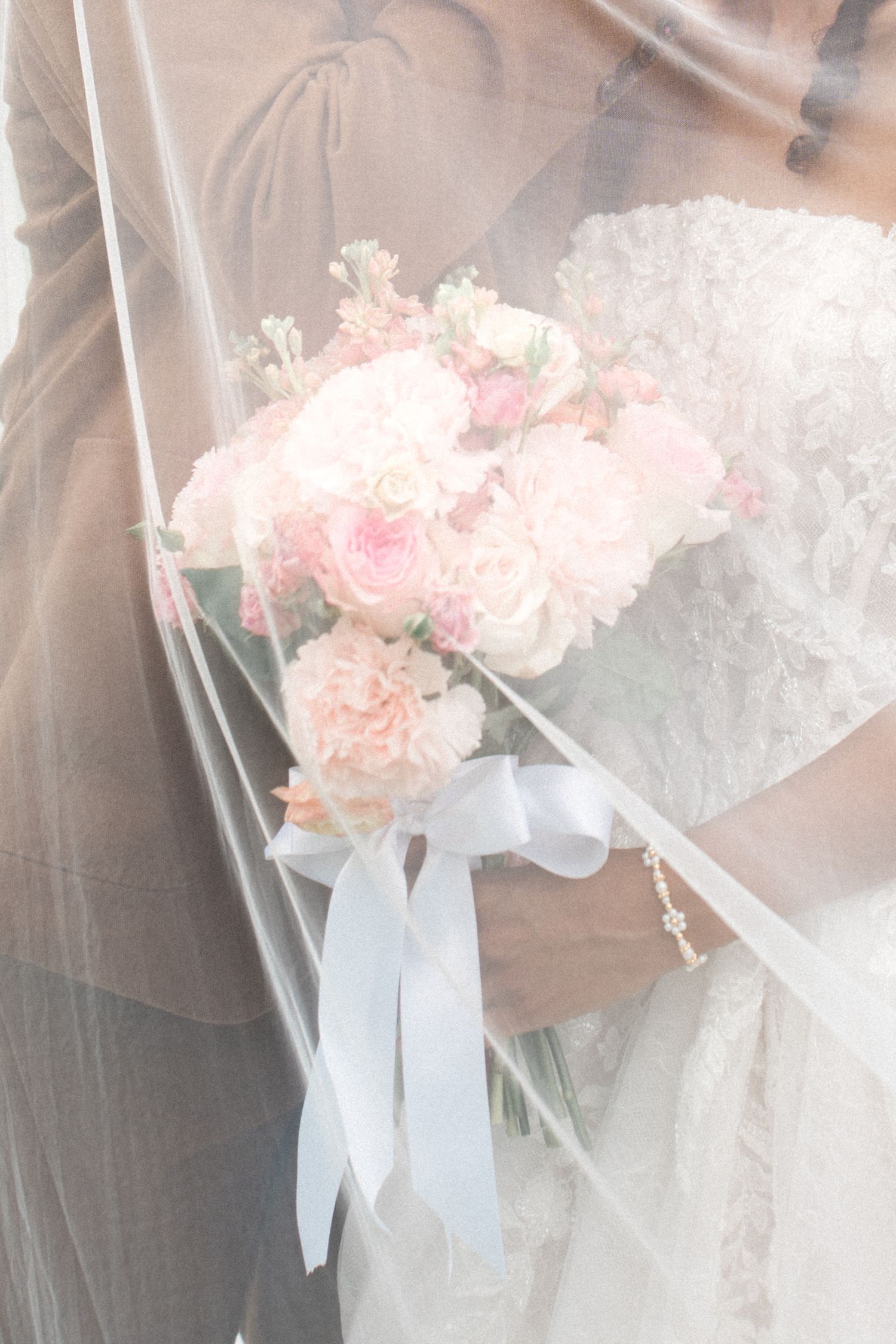 Soft focus wedding bouquet with pink roses and white ribbons through delicate veil.