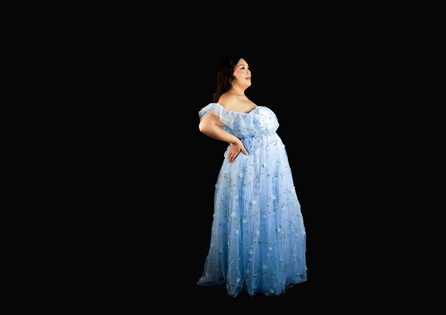 A pregnant woman in a light blue tulle dress against a black background at her luxury maternity photo session in San Antonio
