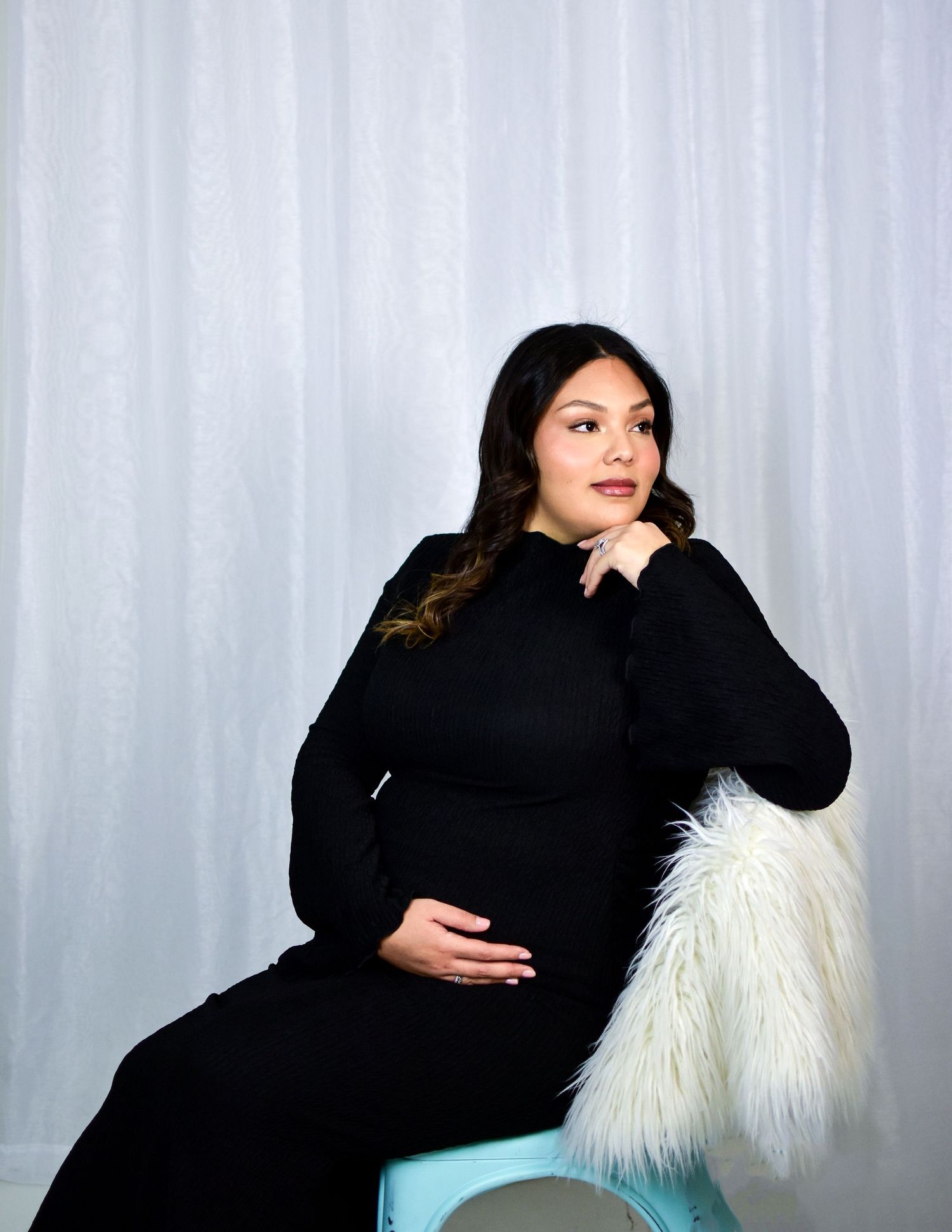 An elegant maternity portrait featuring a woman in black against a light backdrop with fur accent. San Antonio maternity photography