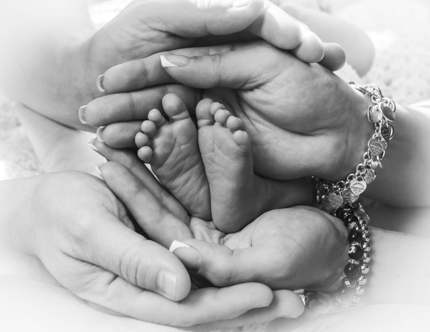 Black and white photo of adult hands cradling tiny newborn baby feet, symbolizing family love and new parenthood.
