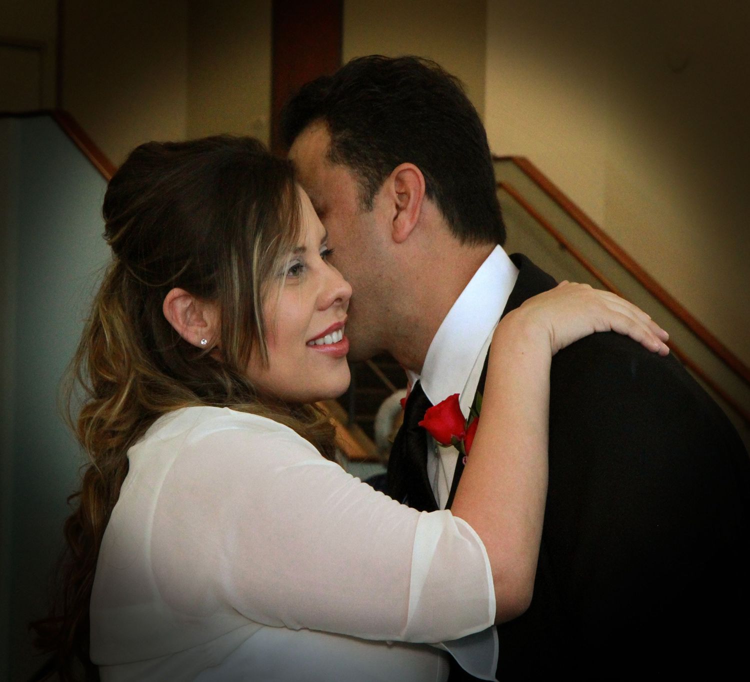 Couple sharing a romantic embrace, man in tuxedo with red bow tie kissing woman in white dress.