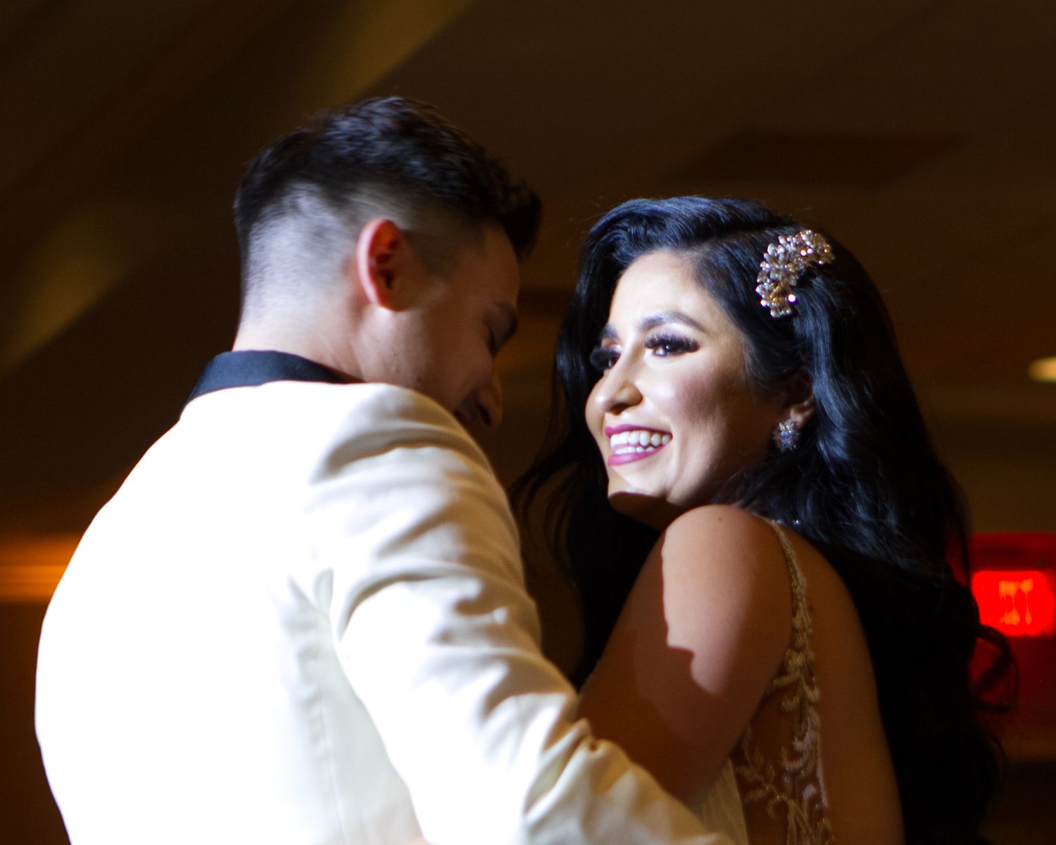 Couple sharing a joyful first dance at wedding reception, bride smiling in elegant attire with floral hair accessory.