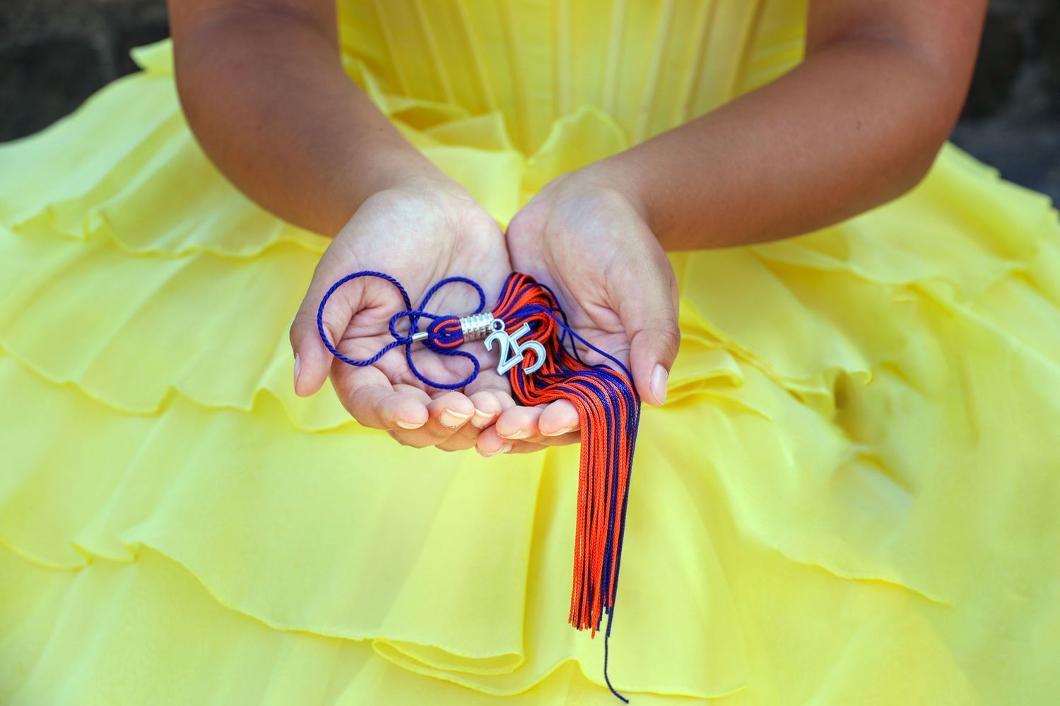 Hands holding a colorful tassel from graduation cap in a soft background at Landa Library in San Antonio Senior Photography session.