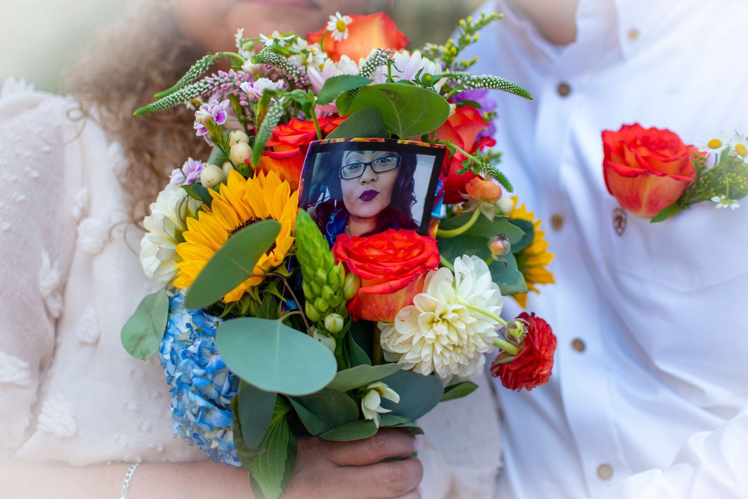 Wedding bouquet with colorful flowers including sunflowers and roses, featuring a memorial photo of a loved one.