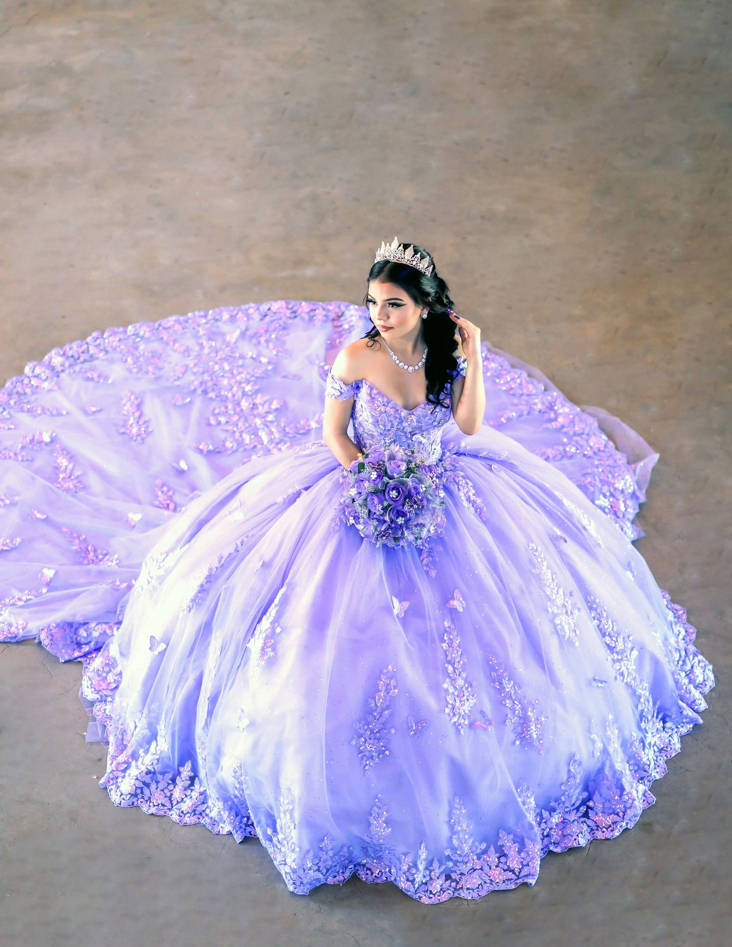 A lavender and white quinceañera dress with intricate beading spreads out in a circular pattern on a concrete floor.
