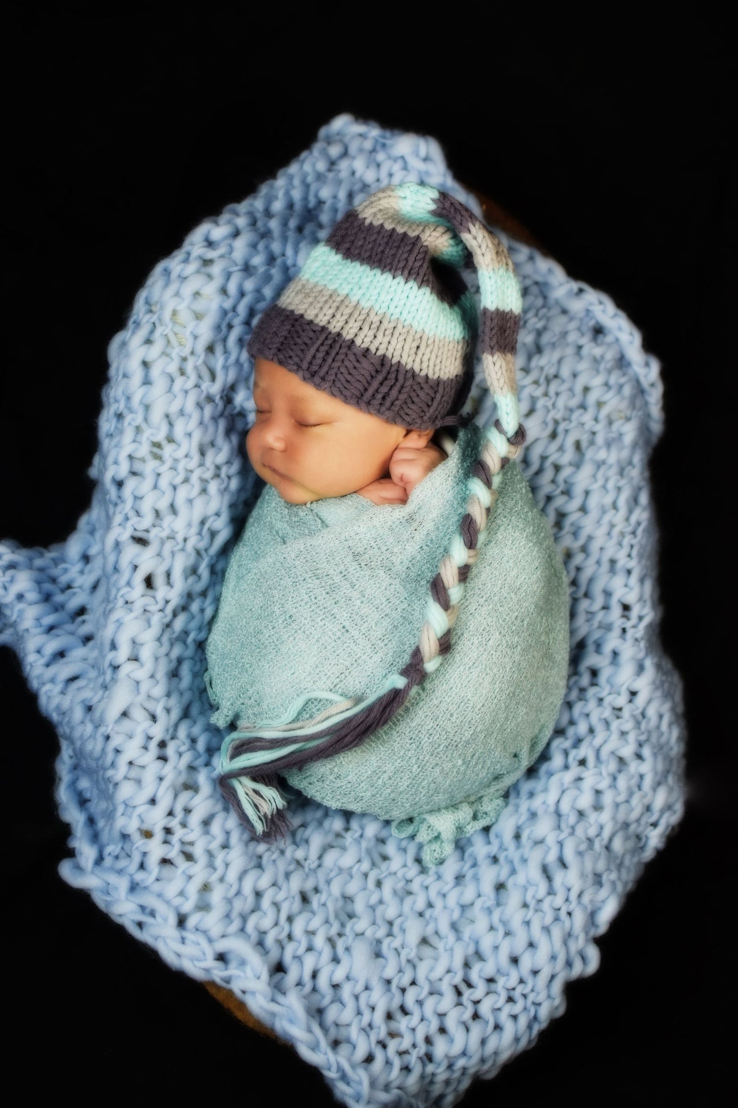 Sleeping newborn wrapped in aqua blanket with striped knit hat on blue background. San Antonio newborn photography