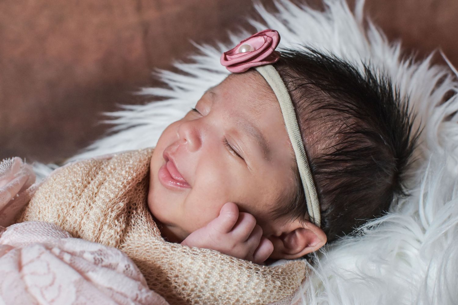 Sleeping newborn baby girl with pink flower headband, wrapped in soft blanket on white fur photographed by Precious Keepsakes Photography SA